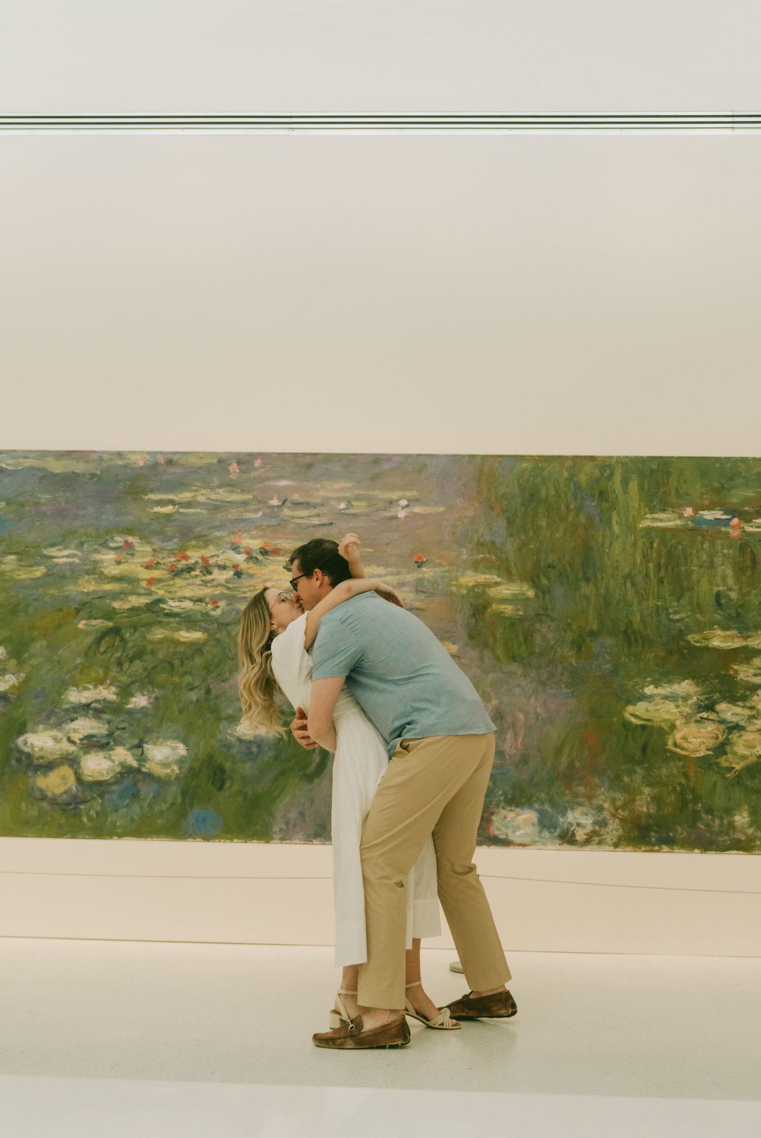 A photographer bends down to capture a close-up shot of water lilies in front of a large Monet painting at a museum.