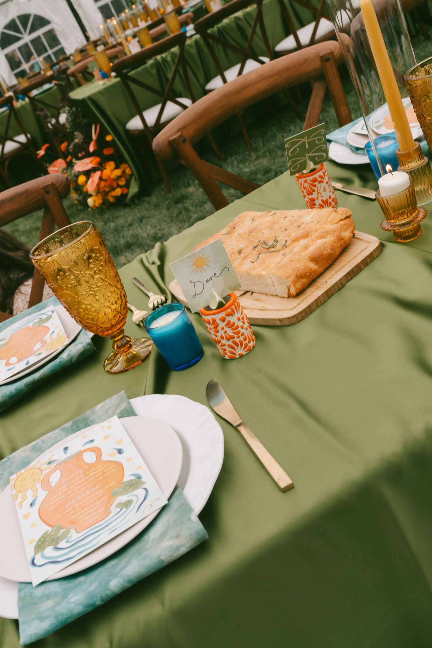 Elegant table setting with amber glassware and peach accents on sage green tablecloth at outdoor event.