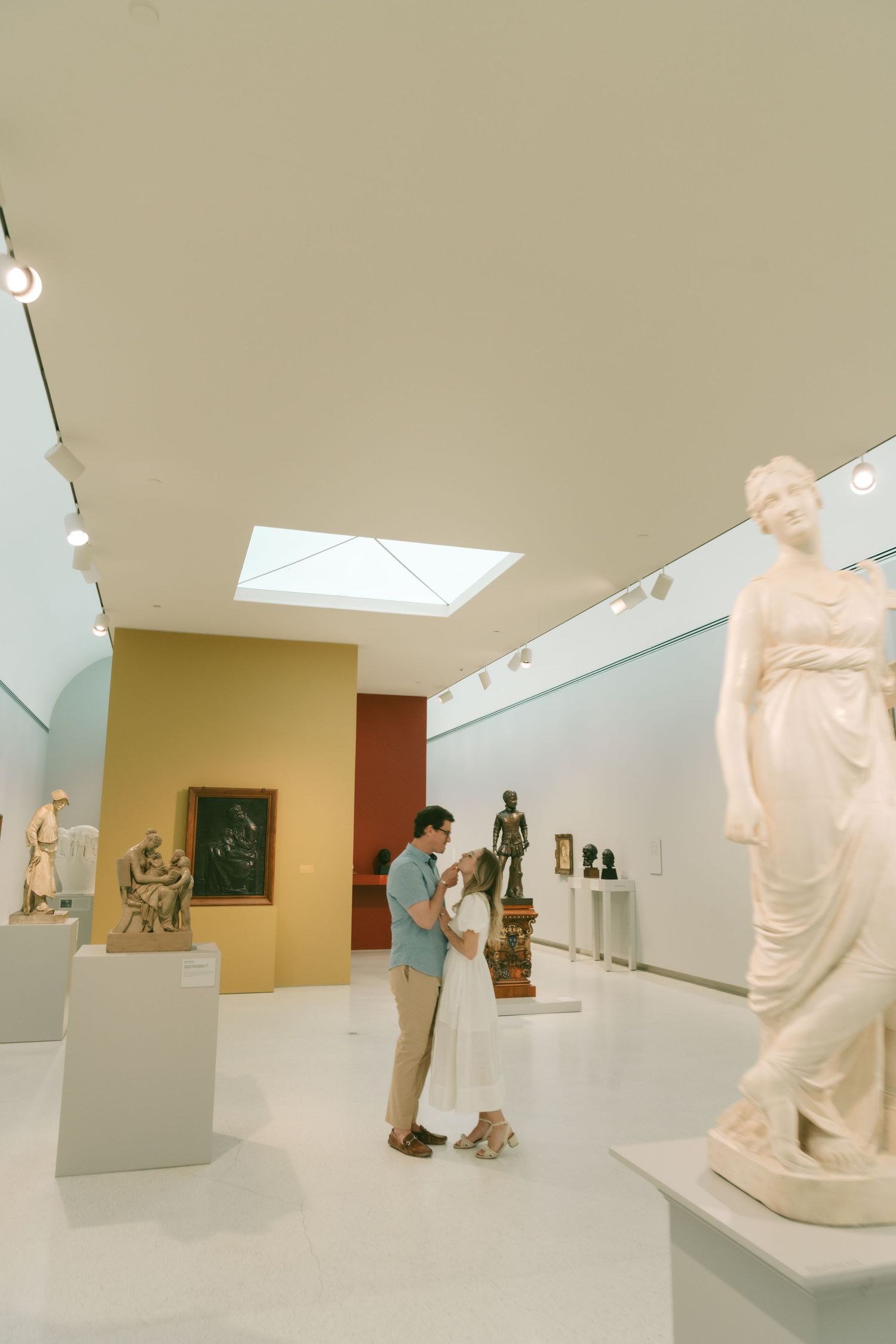 Two people view white marble sculptures in a modern museum gallery with skylights.