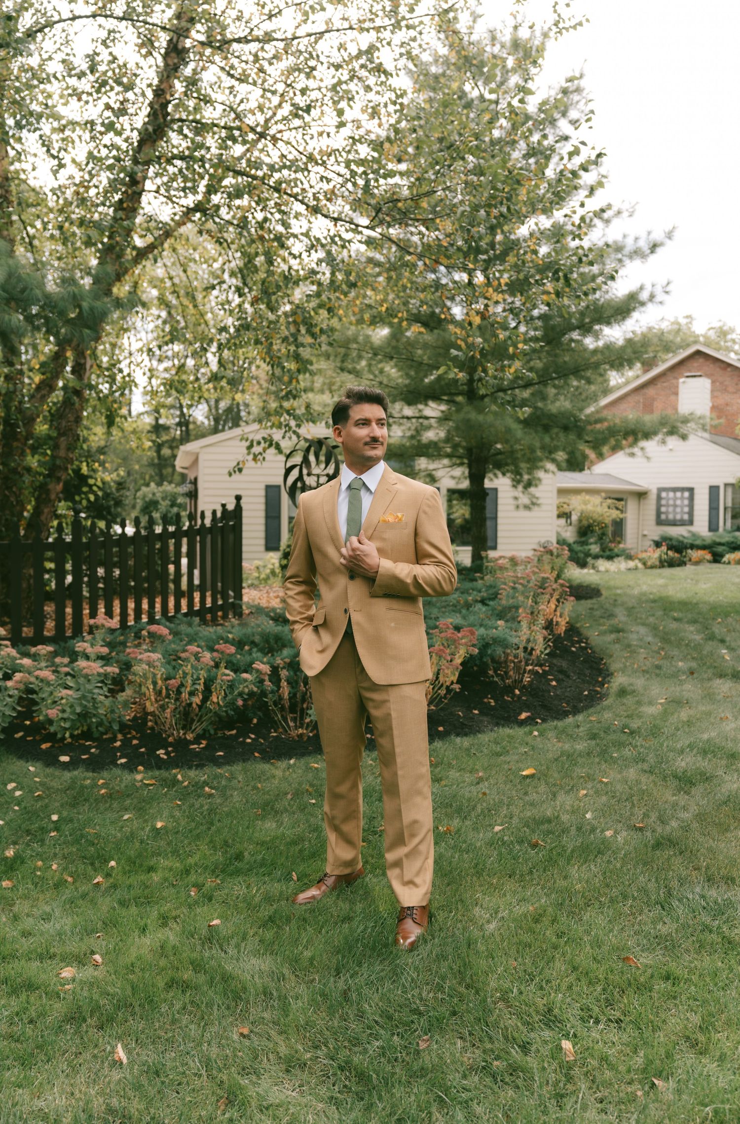 A series of playful jumping poses in a tan suit against a backyard garden setting.