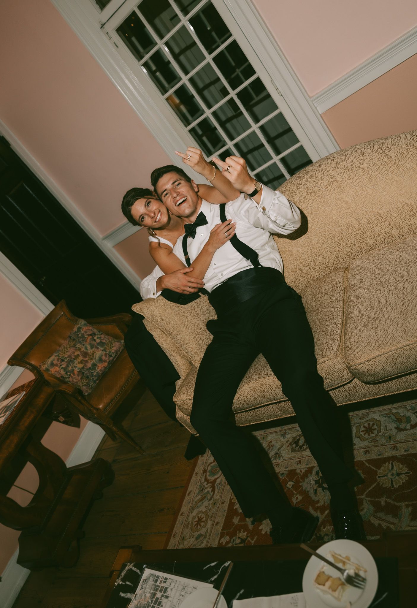 Two people relaxing and posing casually together on a floral patterned couch in a dimly lit room.