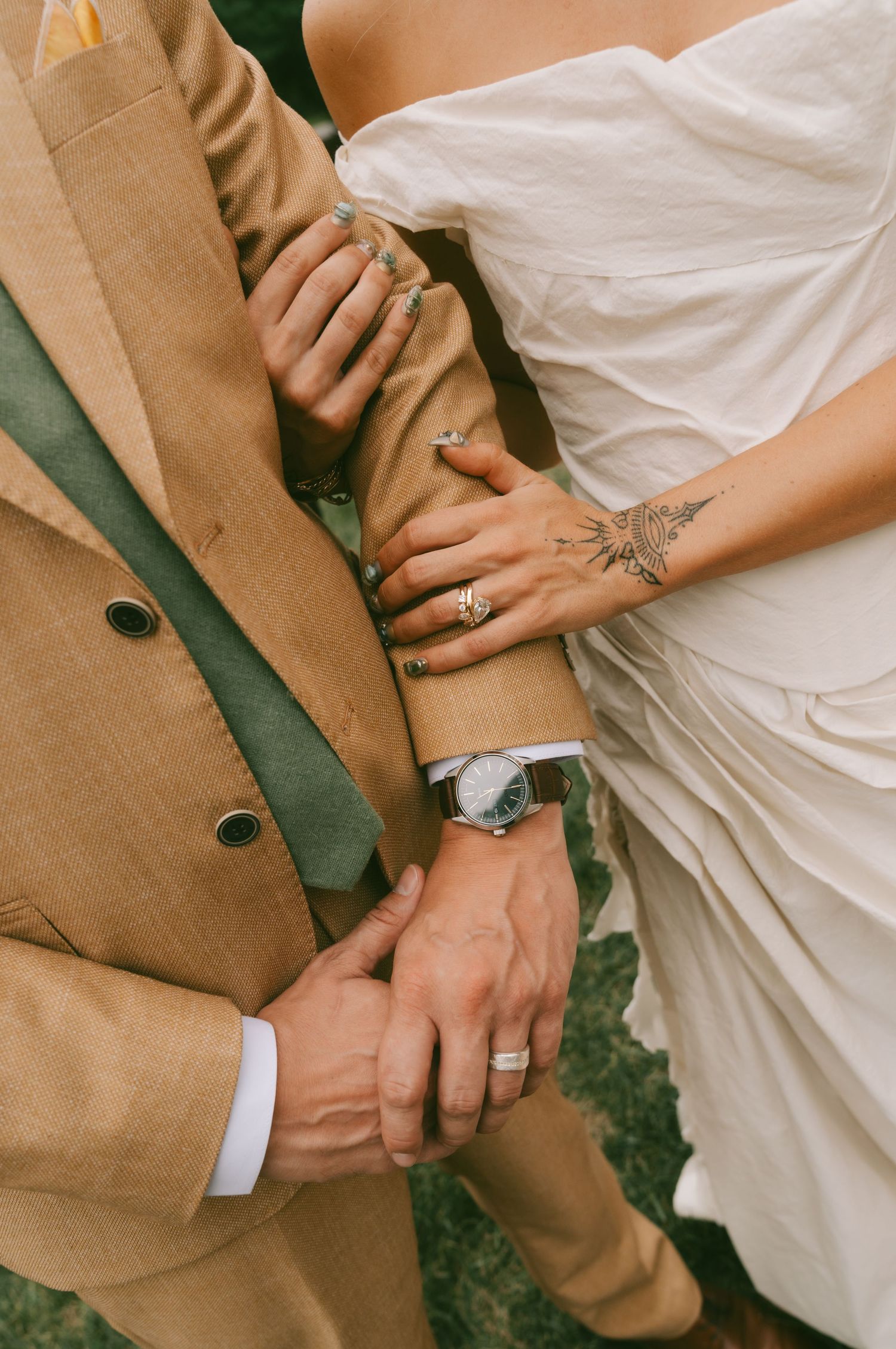 Close-up detail of wedding rings and formal attire in tan and white.