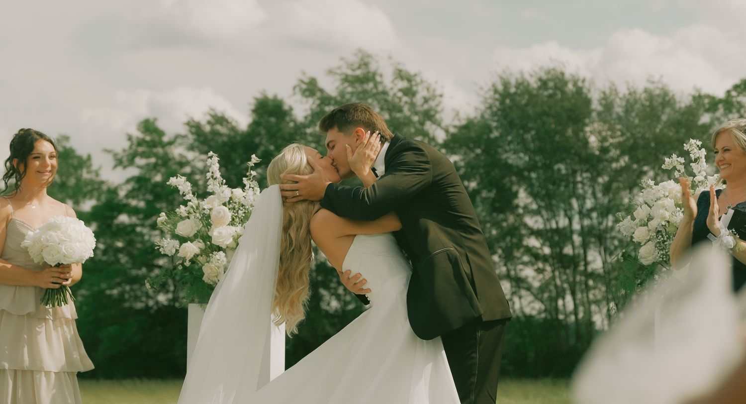 Wedding couple embracing in soft lighting with trees visible in background.
