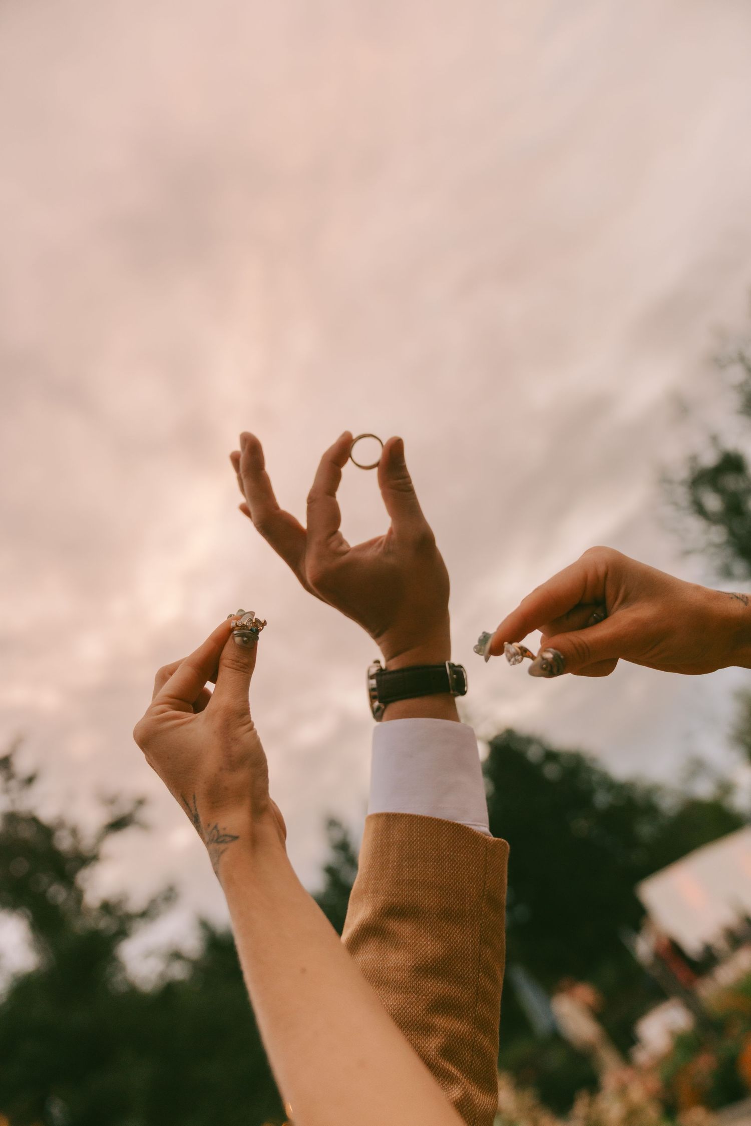 Hands raised against sunset sky showing wedding rings in artistic silhouette composition.
