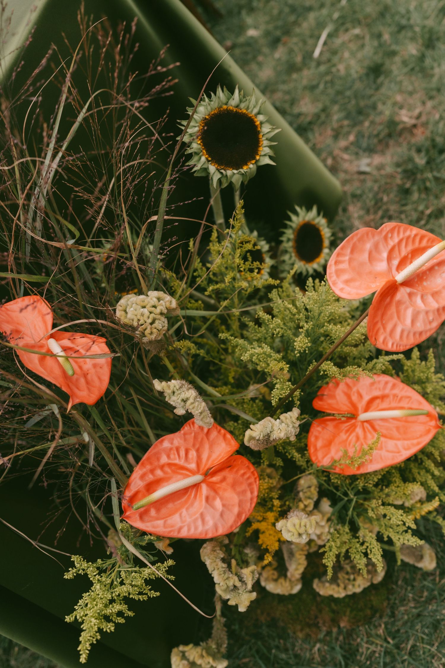 Coral anthurium flowers and sunflowers arranged with greenery in a rustic wedding bouquet.