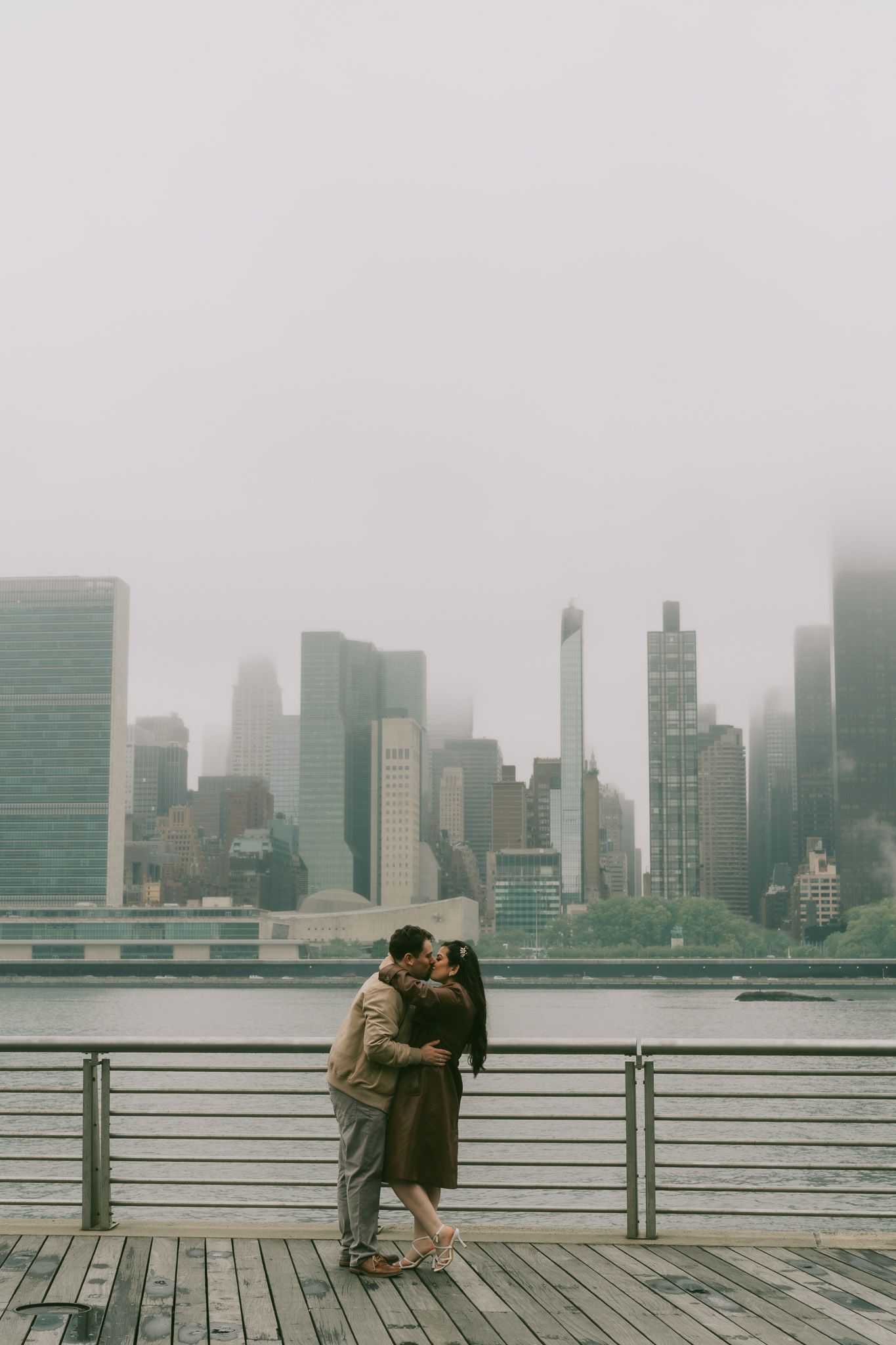 Foggy NYC skyline view with couple embracing on waterfront boardwalk.