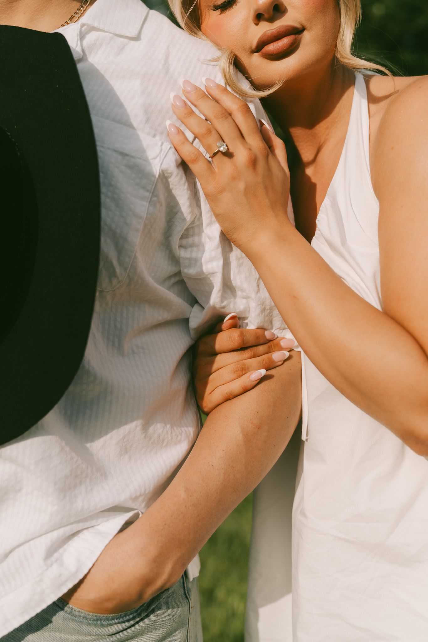 Close-up of hands showing engagement ring against white and black clothing in sunlight.