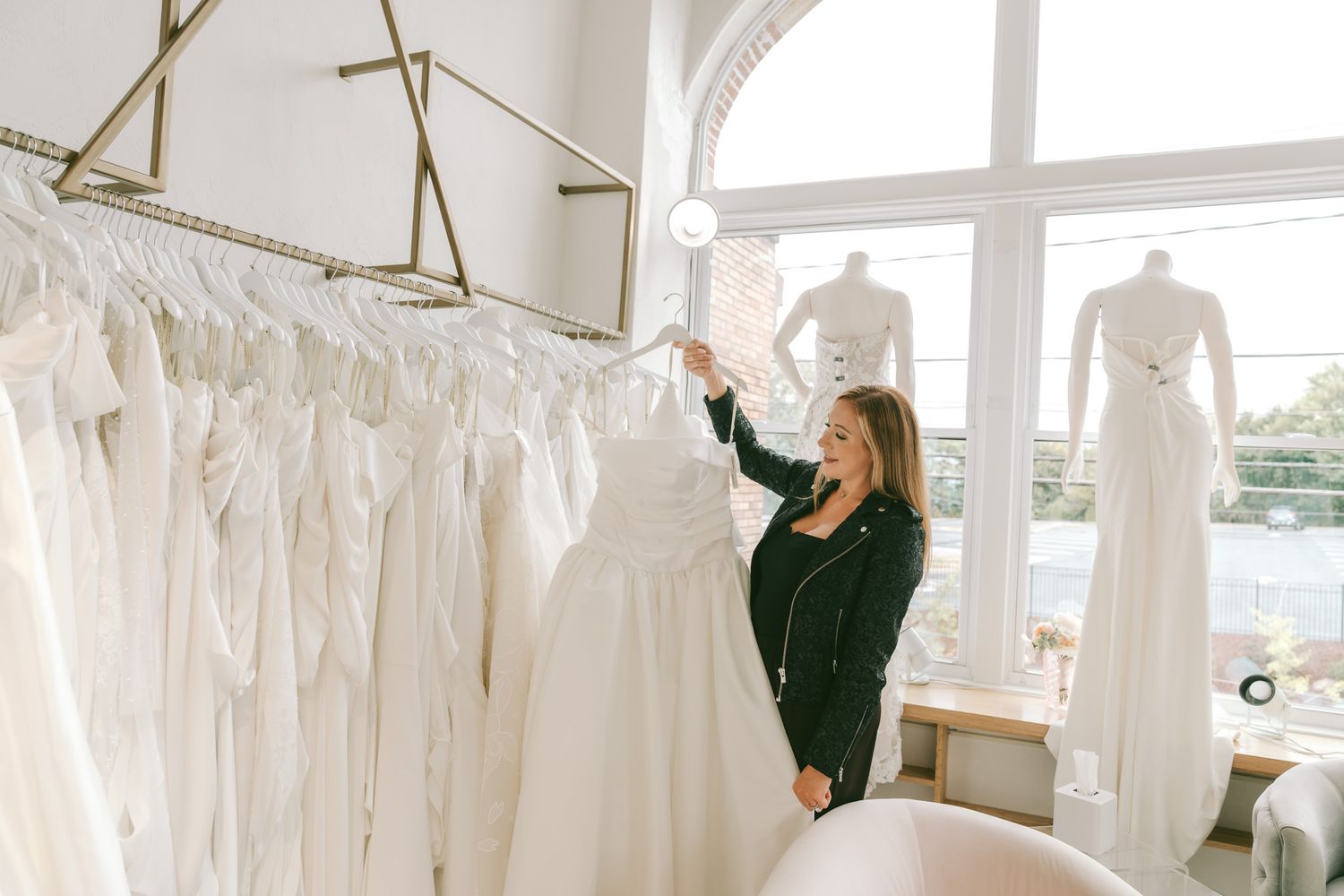 Elegant bridal boutique interior with rows of white wedding dresses displayed on hangers in a bright, airy showroom.