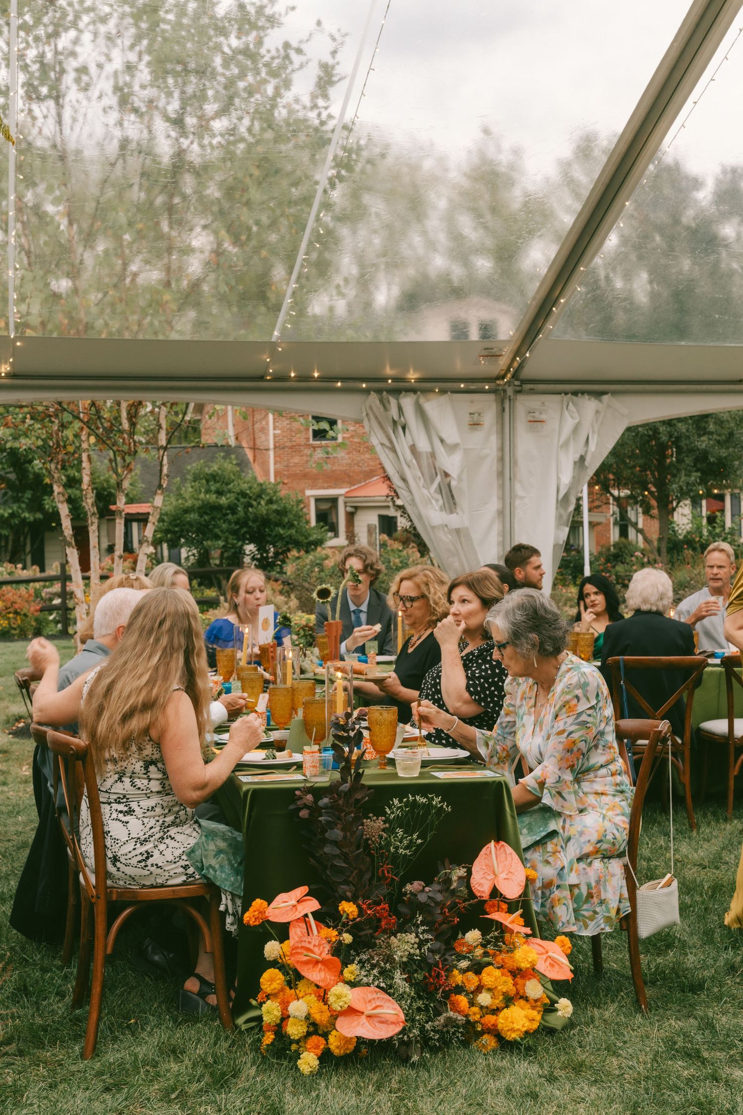 Guests mingle and socialize at an outdoor garden party with floral arrangements of orange and yellow blooms.