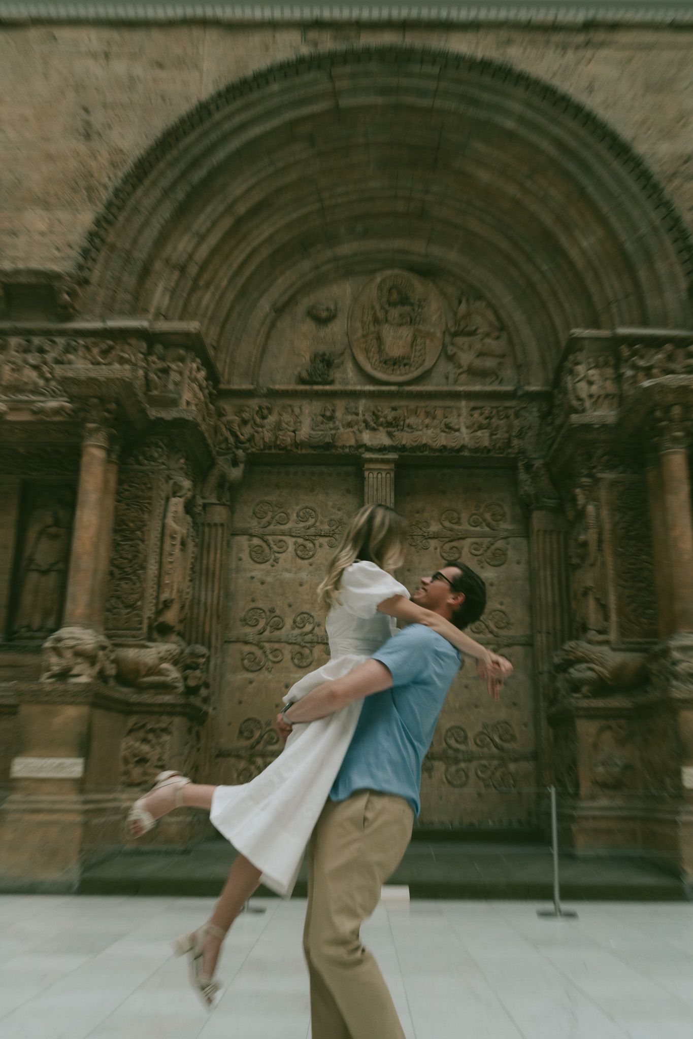 Romantic moment captured in front of an ornate stone church archway with intricate carvings.