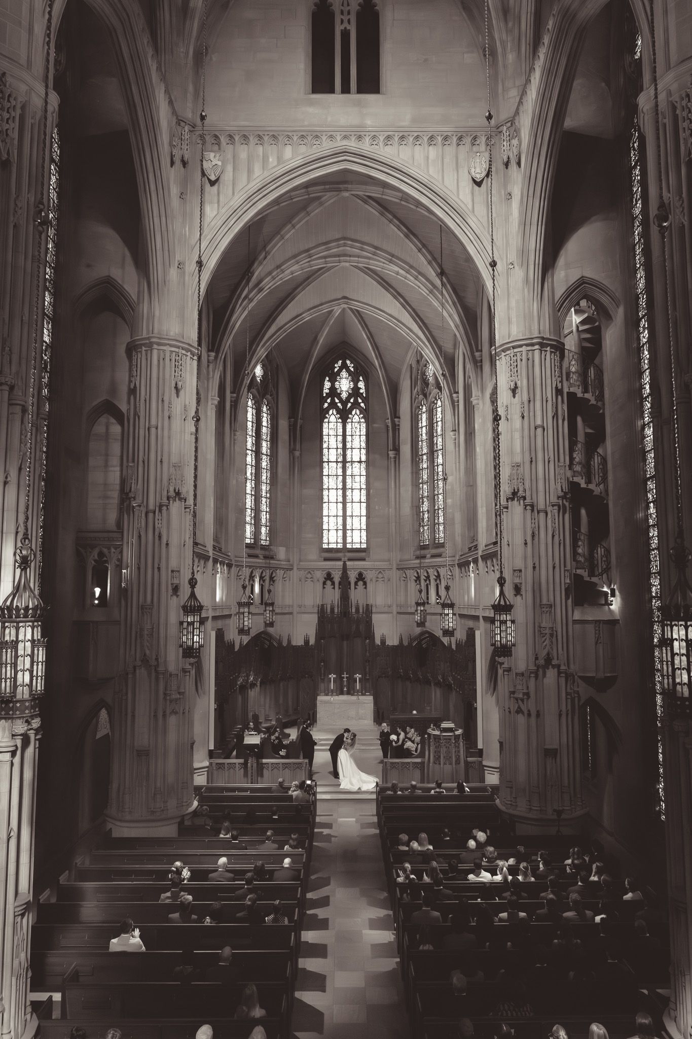 Interior panoramic view of a Gothic church with vaulted ceilings, arched windows, and wooden pews in black and white.