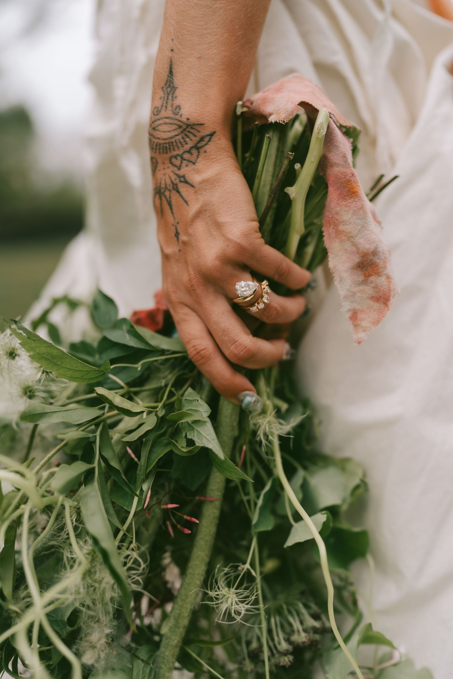 Close-up of hands holding a rustic wedding bouquet with green foliage and delicate white flowers.