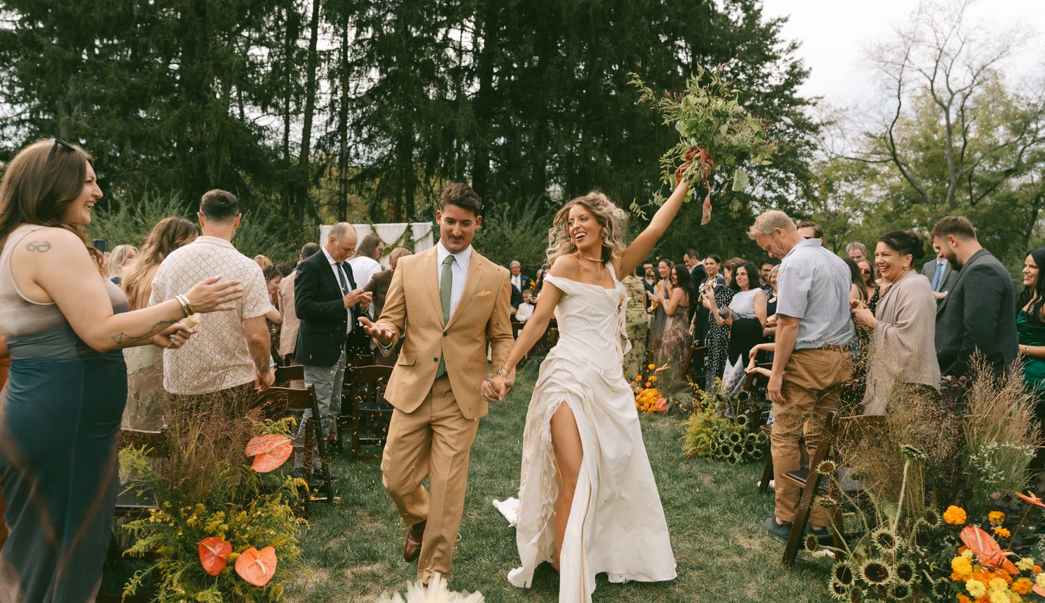 A wedding party celebrates outdoors in a garden setting with orange floral decorations and khaki suits.