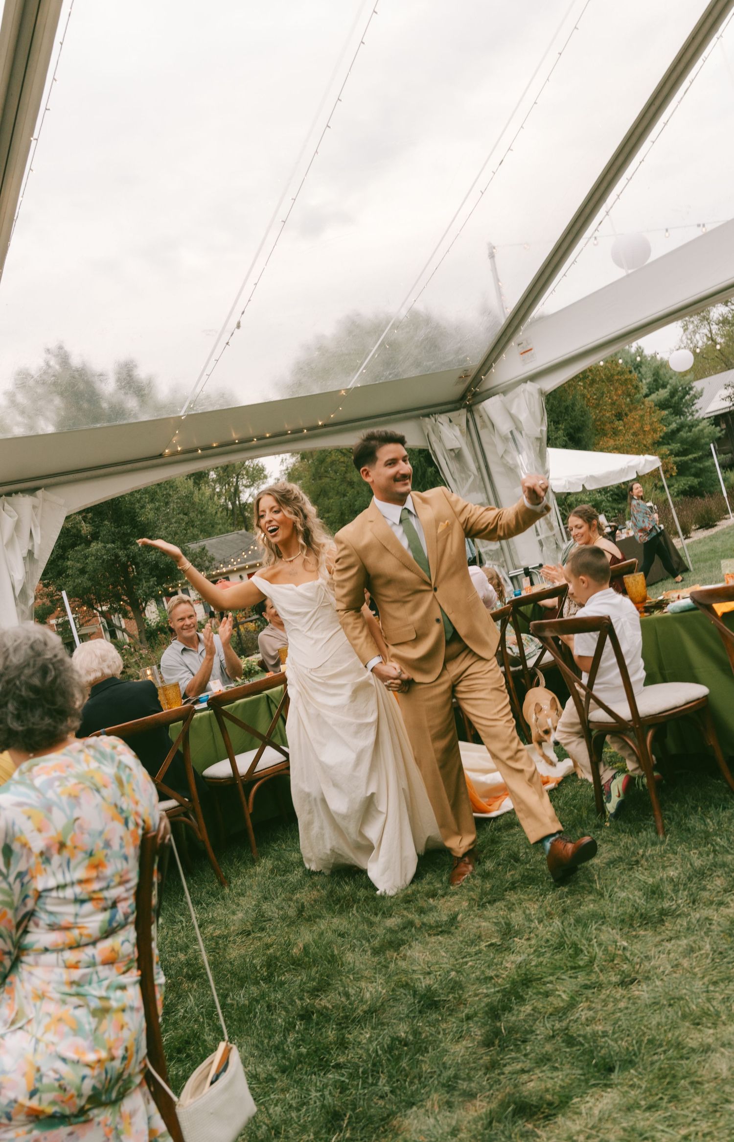 Wedding guests dance and celebrate joyfully under a white tent at an outdoor reception.