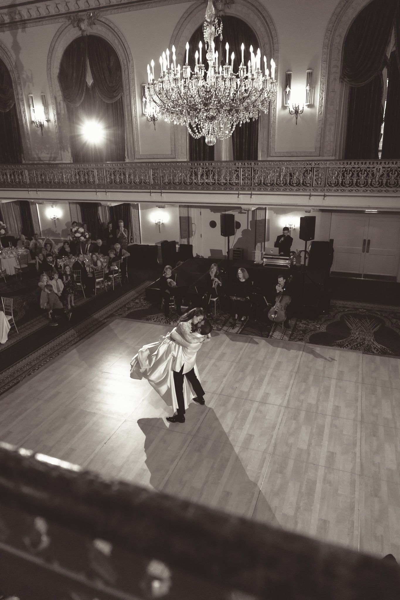 Couple dancing in an elegant ballroom with crystal chandeliers and wooden floors during a formal event.