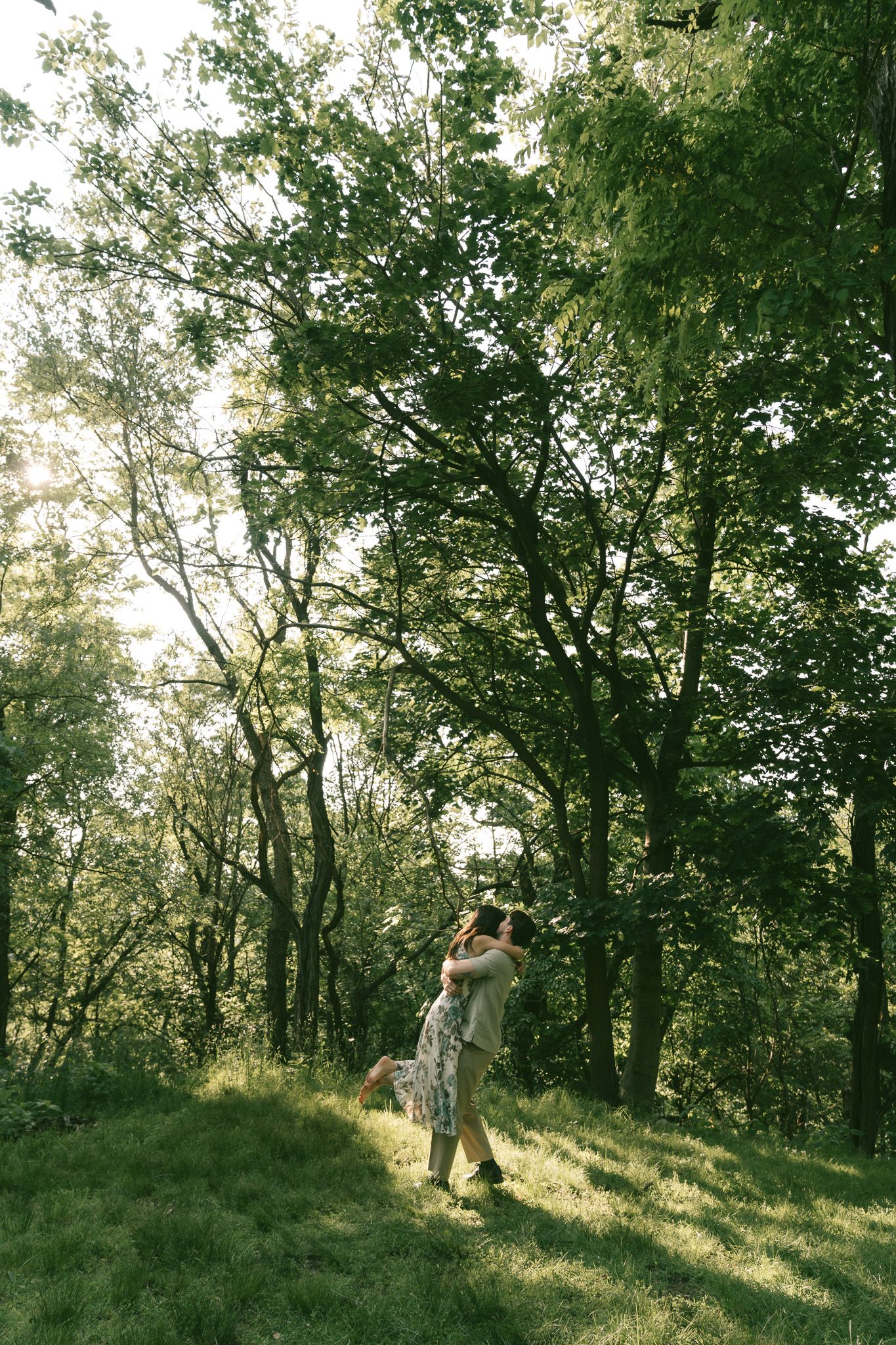 couple twirls in a sunlit forest glen while rays of sunlight filter through lush green trees creating an ethereal atmosphere in Shenley park