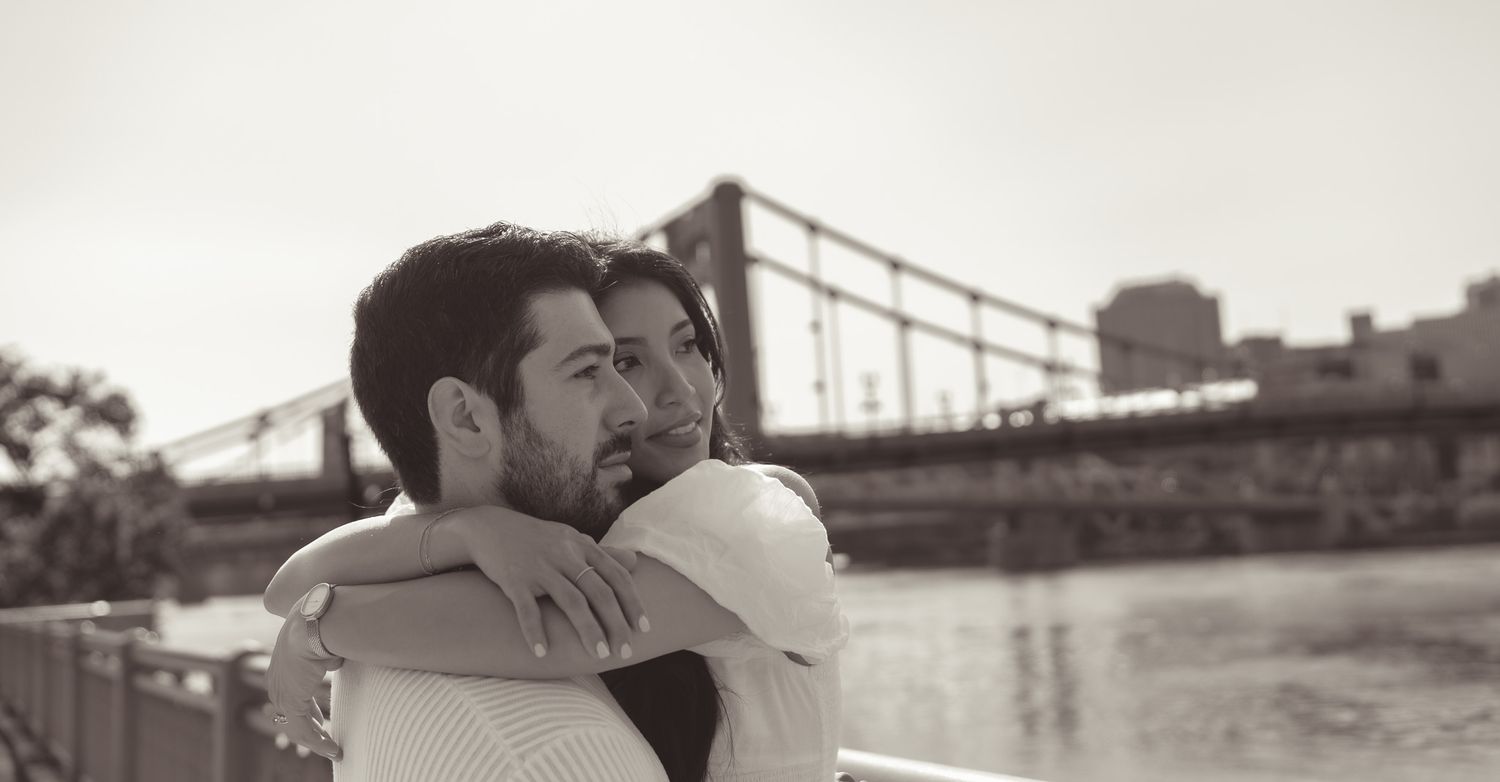 A black and white romantic moment captured with a bridge in the background at sunset in north shore, pittsburgh.