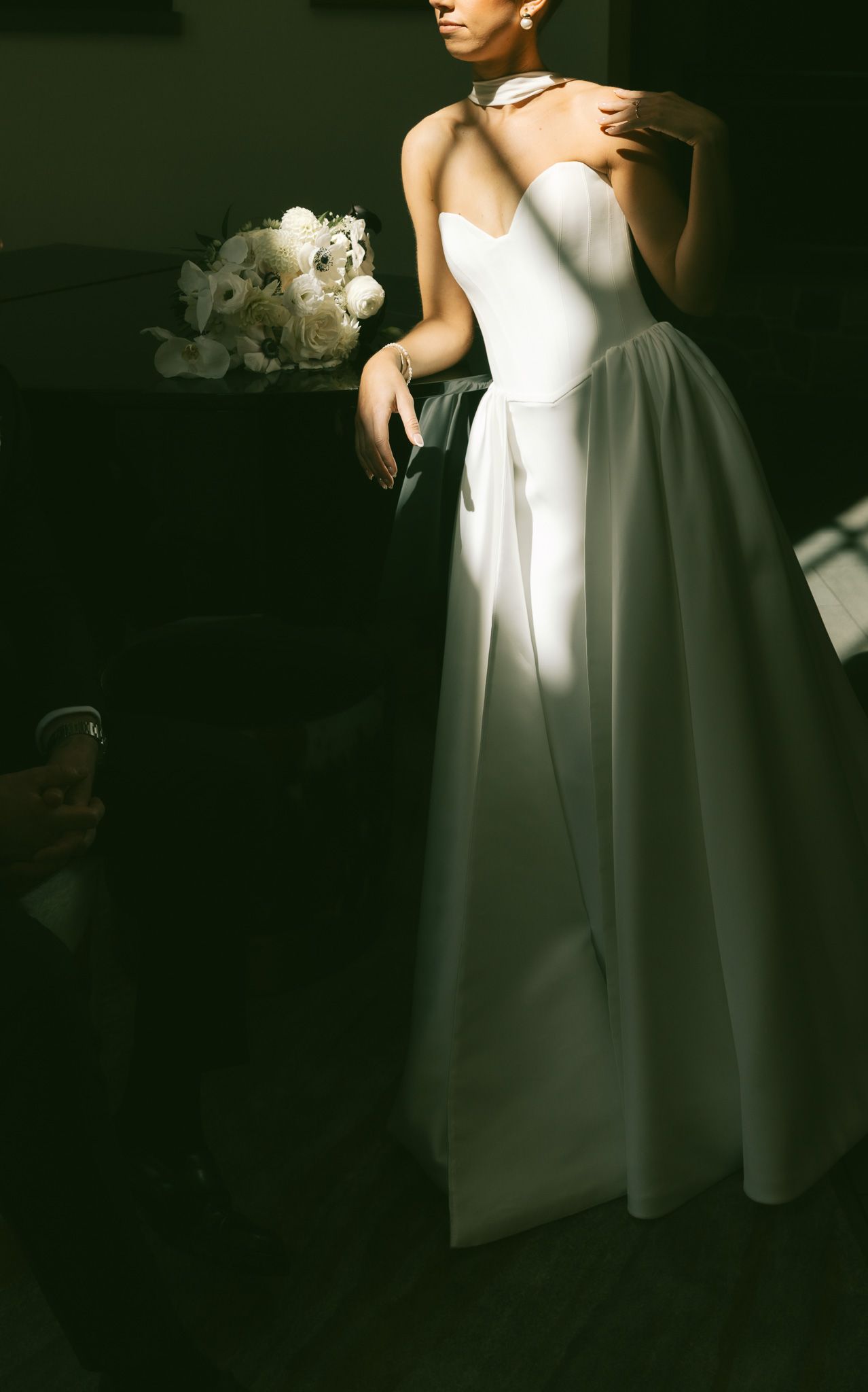 Elegant white wedding dress with sweetheart neckline and full skirt photographed in dramatic lighting with white bouquet.
