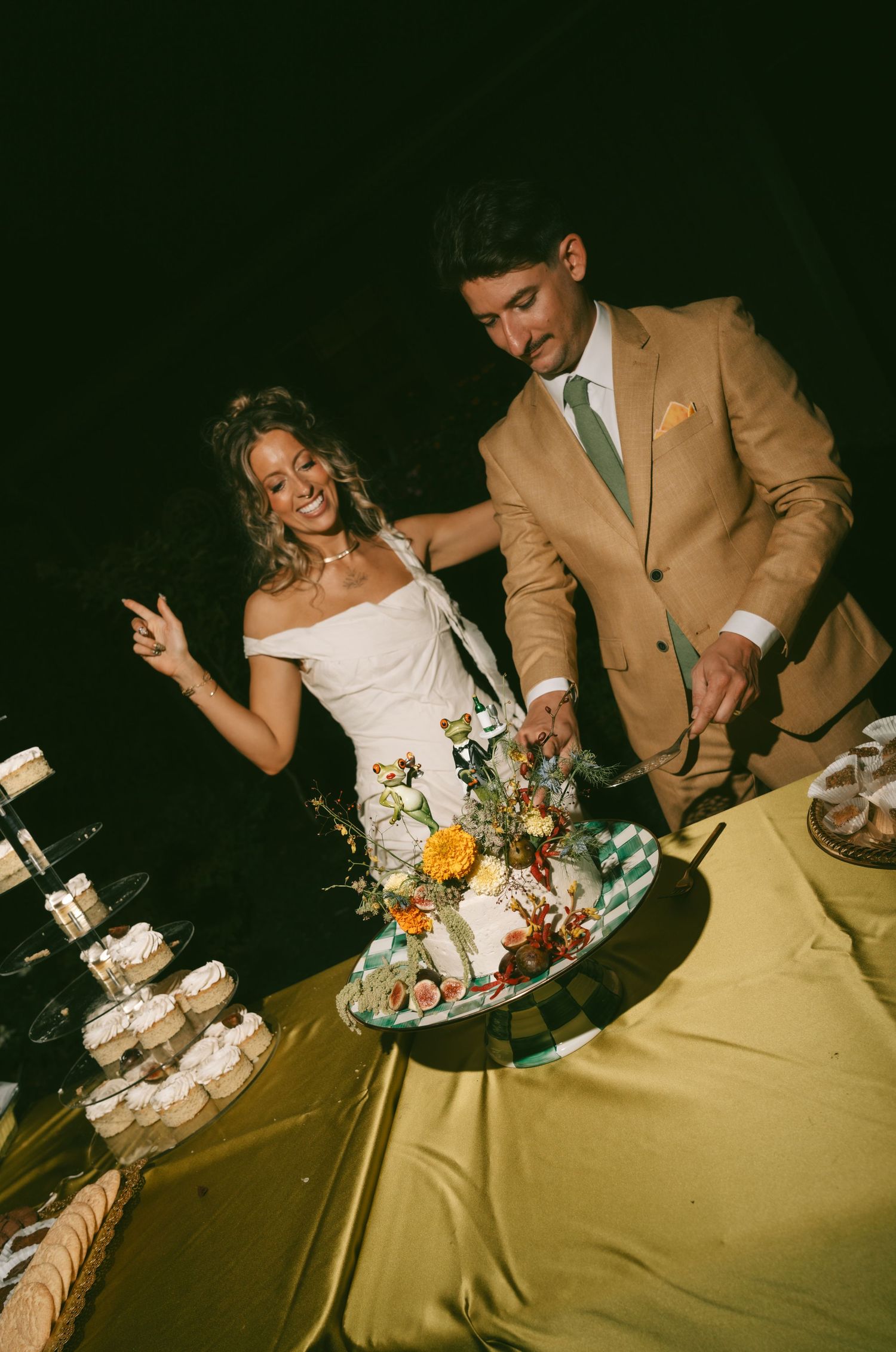 A couple in wedding attire playfully cuts their tiered wedding cake together at their reception.
