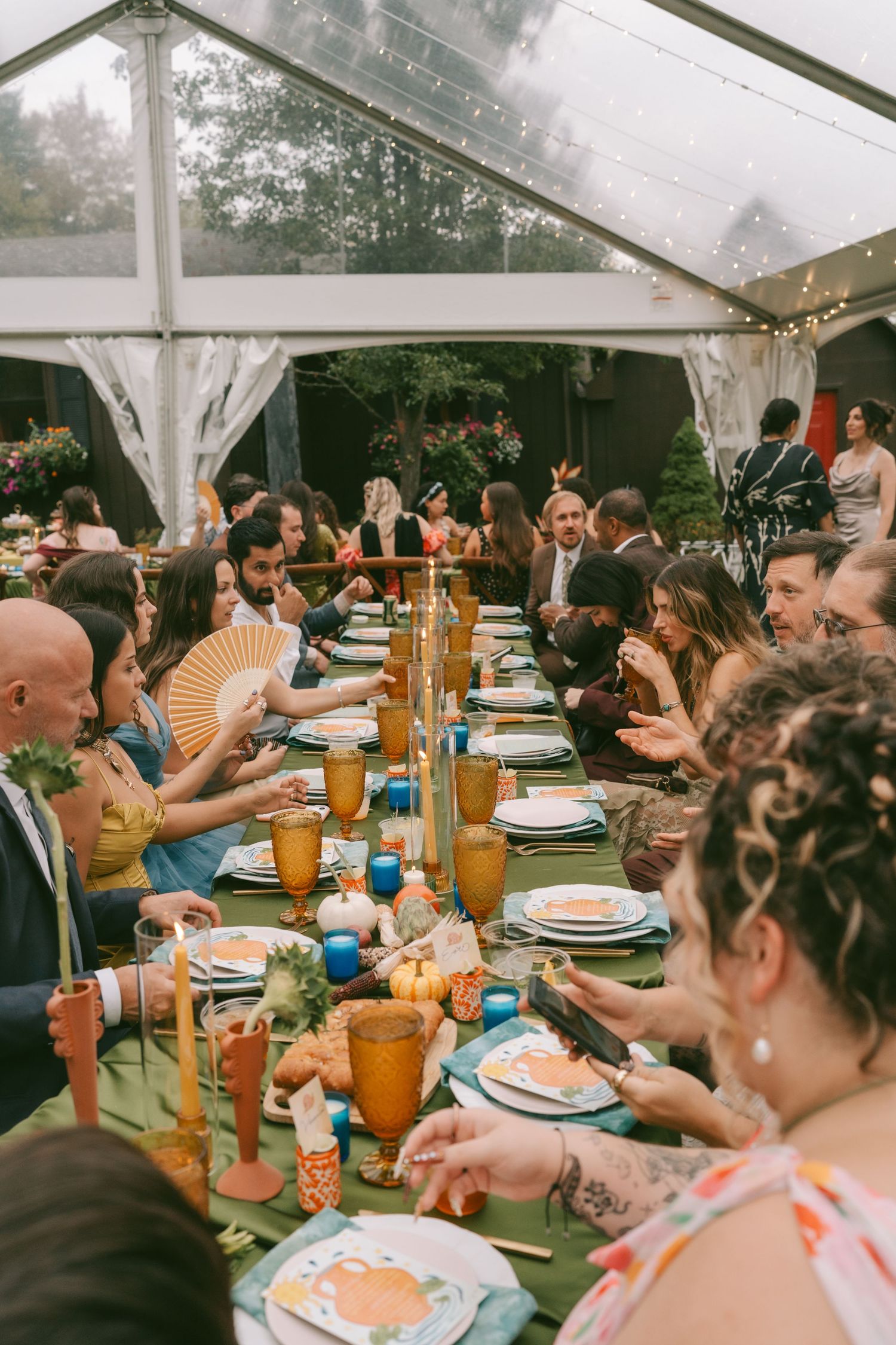 Wedding reception under white tent with guests seated at decorated tables enjoying dinner.