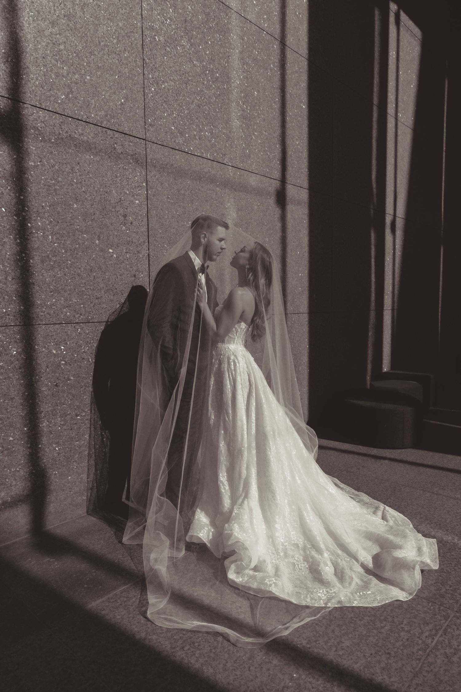 Black and white wedding photo series showing a bride's flowing white dress in dramatic shadows against a stone wall.