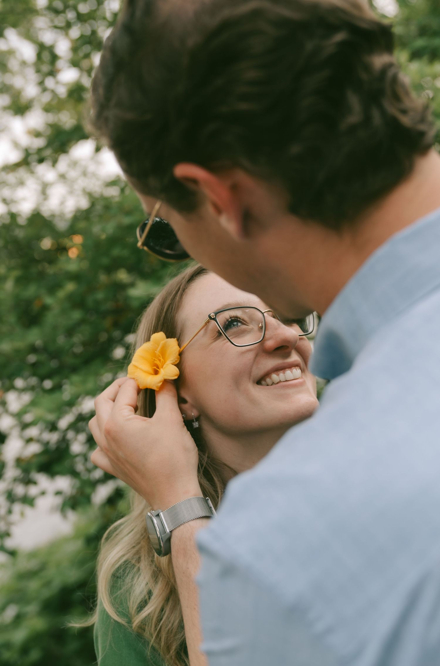 A tender romantic moment captured outdoors as a couple shares a sweet gesture with a yellow flower in nature.