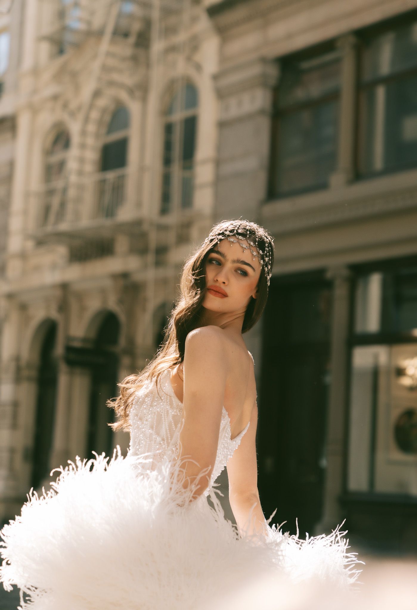 Close-up fashion portrait of a bride in a white feathered dress against a classic architectural backdrop.