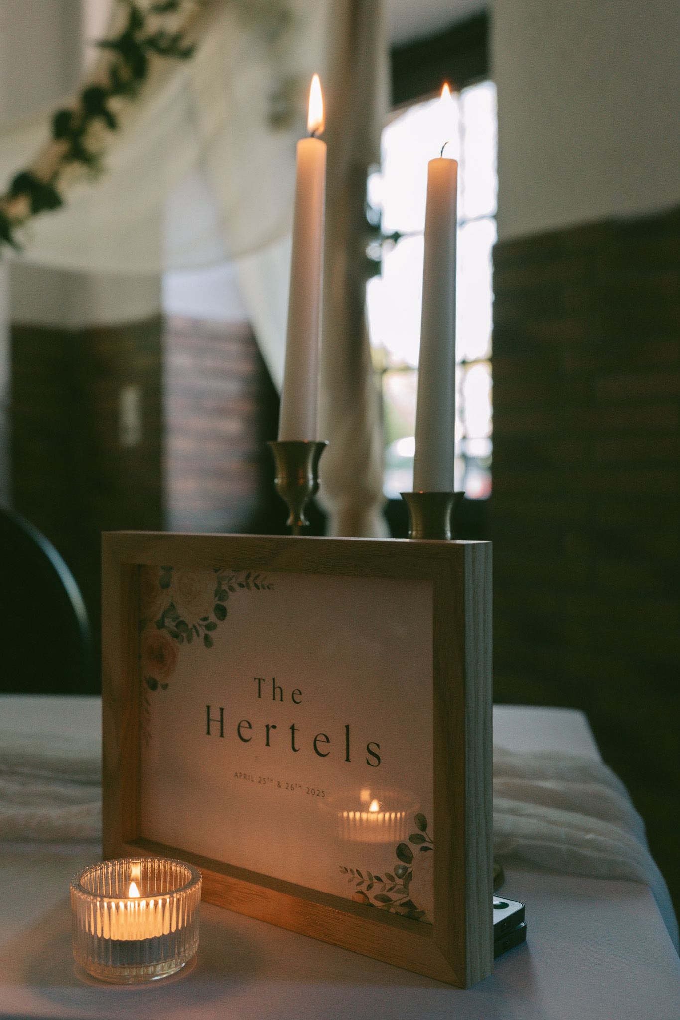 Wedding reception table decor with lit candles and personalized 'The Hertels' sign.