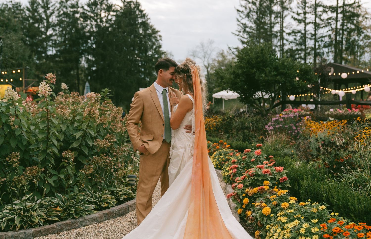 Panoramic view of an outdoor garden wedding venue with orange flowers and string lights.