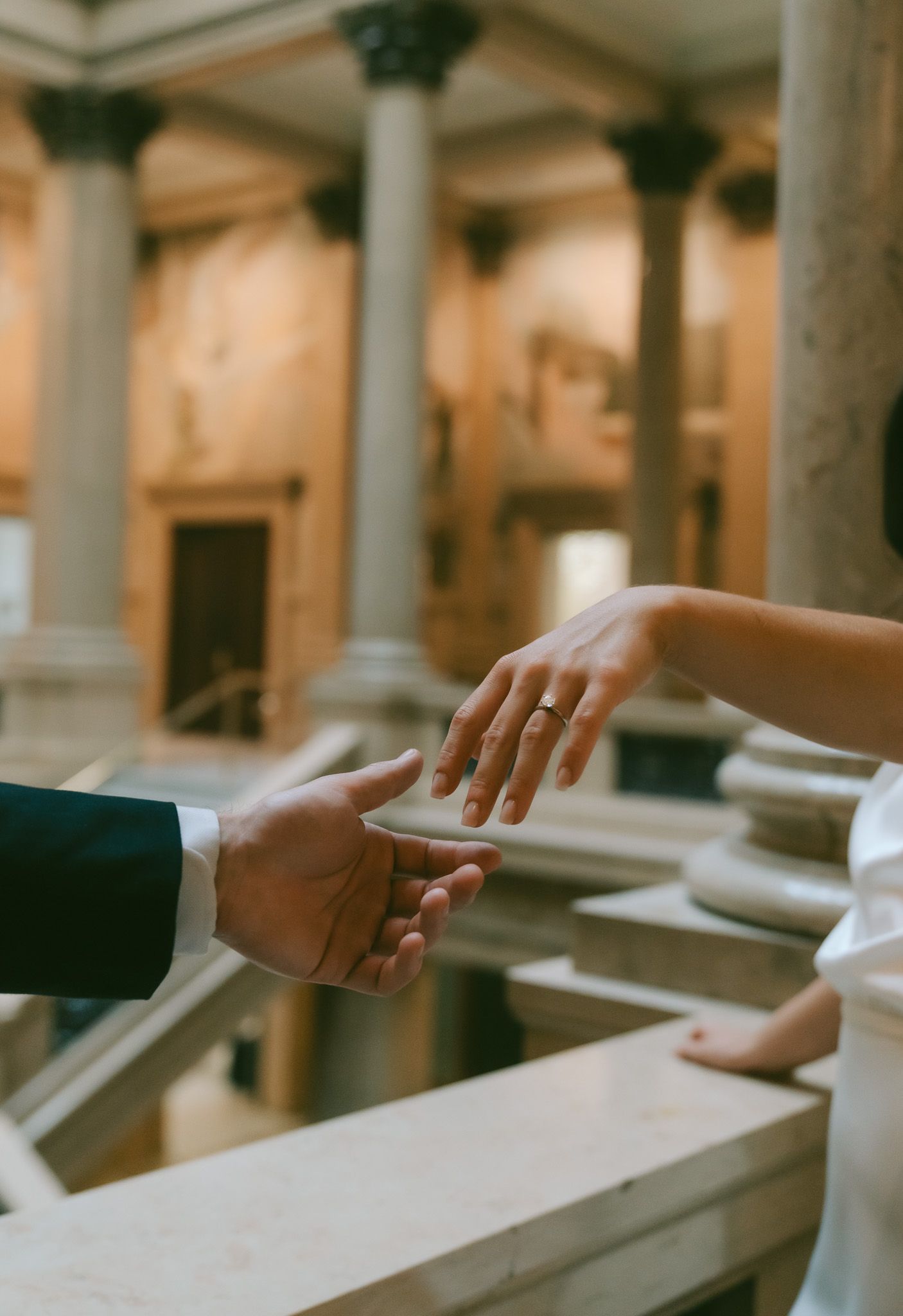 Two hands sliding along an elegant stone banister in a classical architectural setting with columns in soft lighting in carnegie museum.