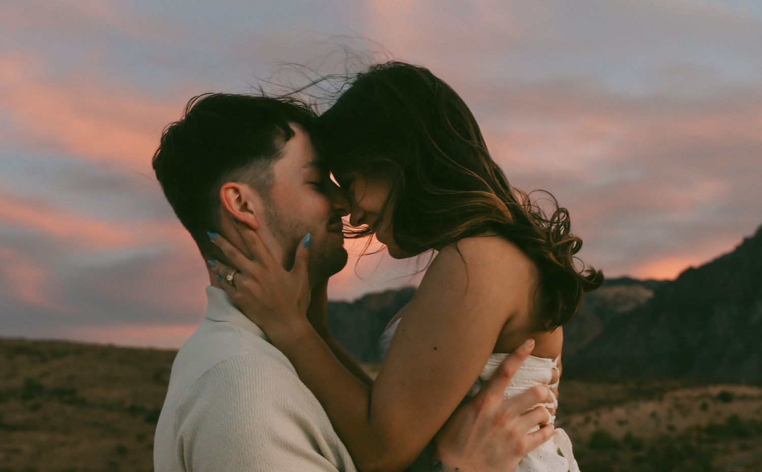 A couple embraces passionately during sunset with a dramatic orange sky and mountains in the background in red rock canyon las vegas, NV.