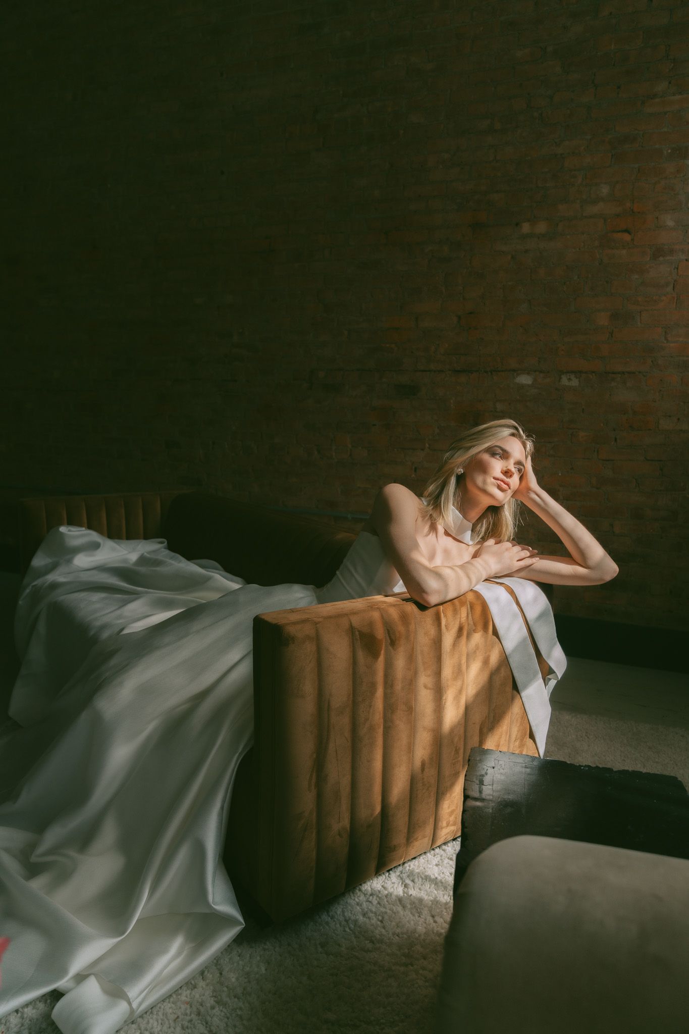 Artistic bridal portrait in a moody setting with flowing dress and exposed brick walls.