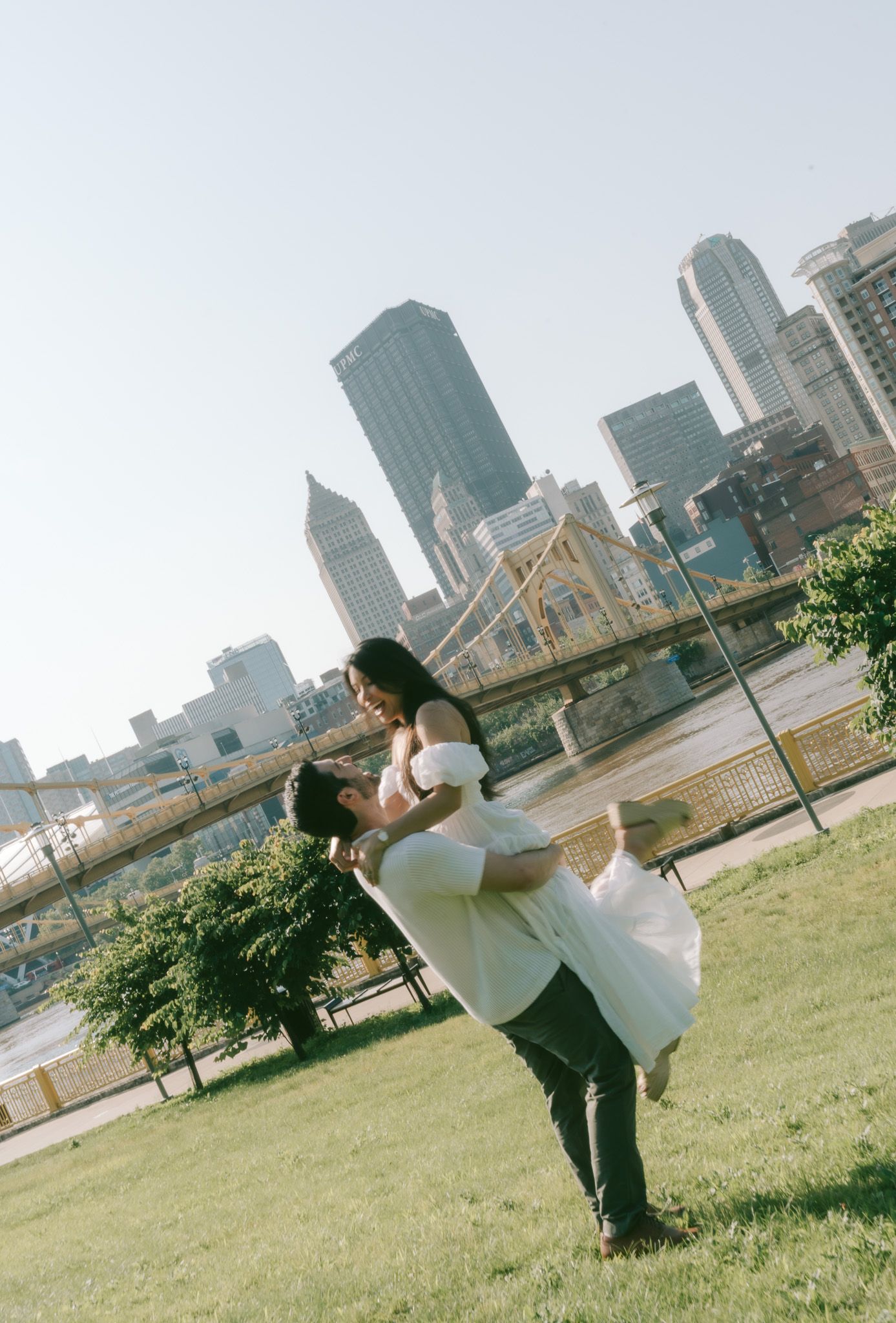 A romantic moment between a couple with Pittsburgh's downtown skyline and yellow bridge creating a stunning urban backdrop in north shore.