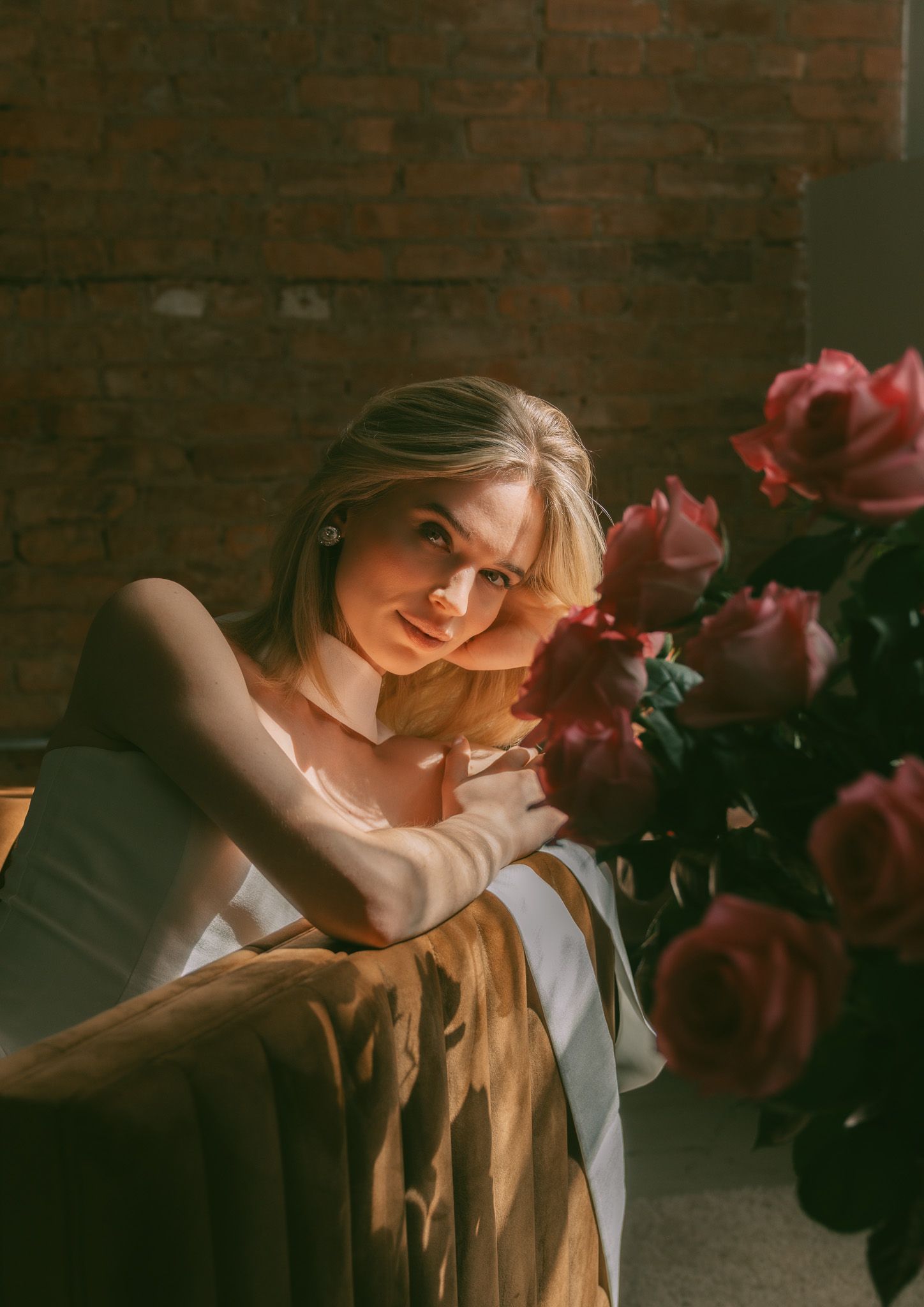 Artistic portrait with warm lighting featuring roses and a white dress against exposed brick walls.