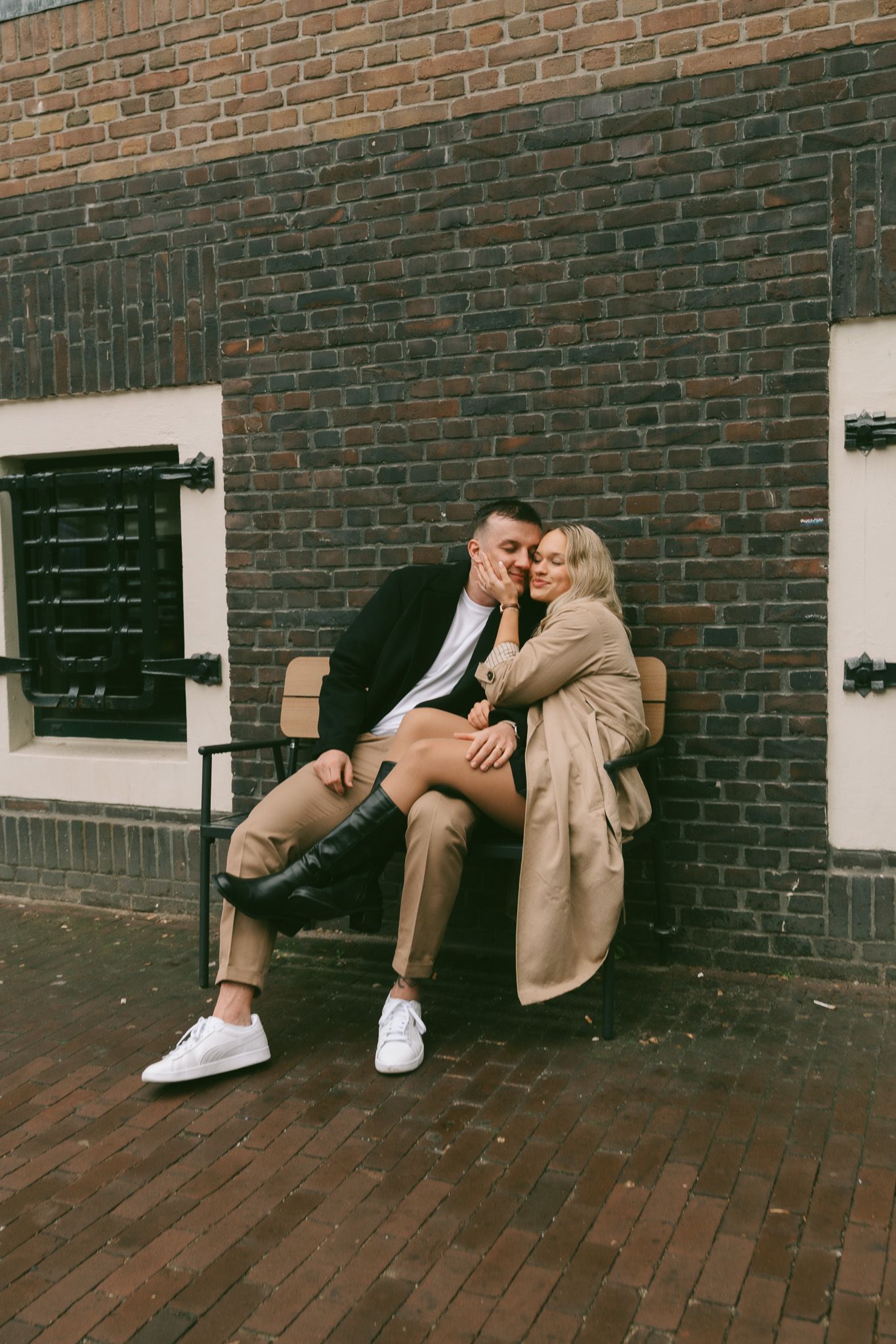 Playful couple's photoshoot against rustic brick wall with green shutters in the streets of Amsterdam.