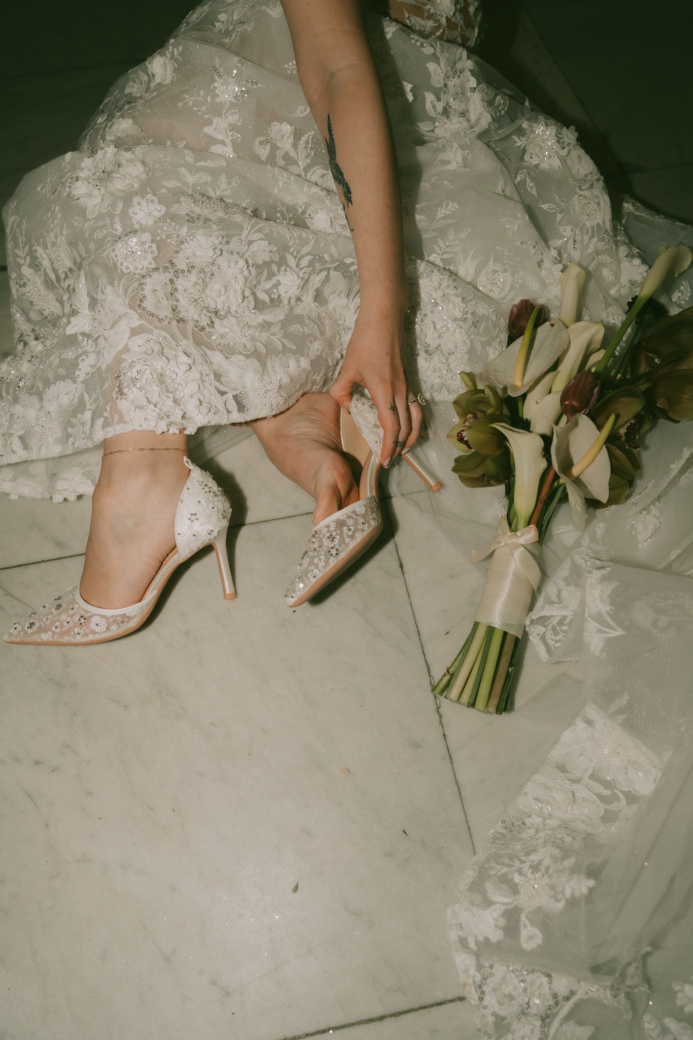 Close-up of bride adjusting sparkly wedding heel next to white floral bouquet.