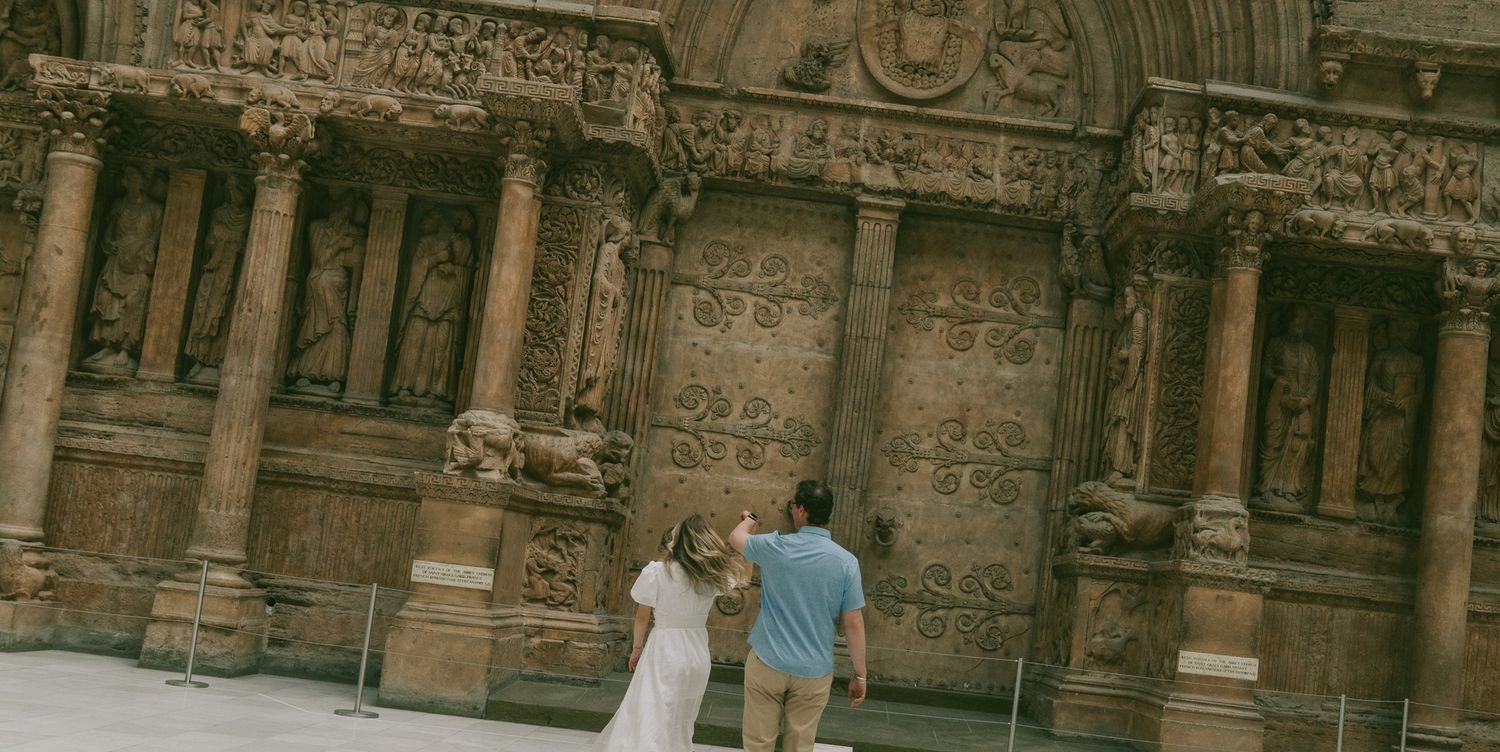 Wedding couple walking near ornate historic building with detailed stone architecture.