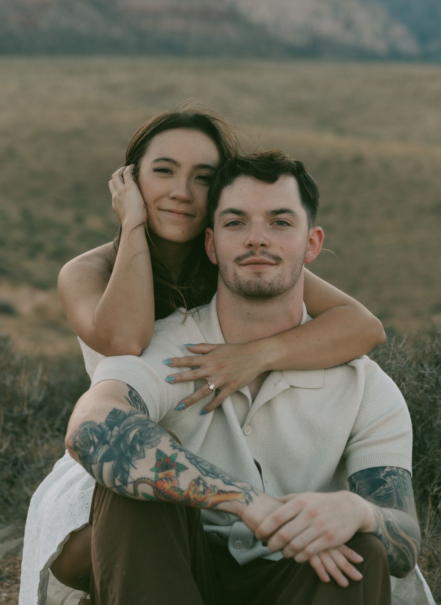 A couple embraces in a moody outdoor setting with desert mountains in the background, creating an intimate portrait in red rock canyon, NV.