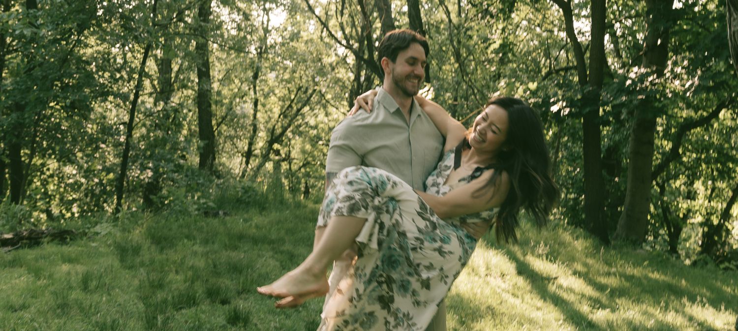 Two people dance and laugh together on a grassy hillside surrounded by trees in warm afternoon light at shenley park, pittsburgh.