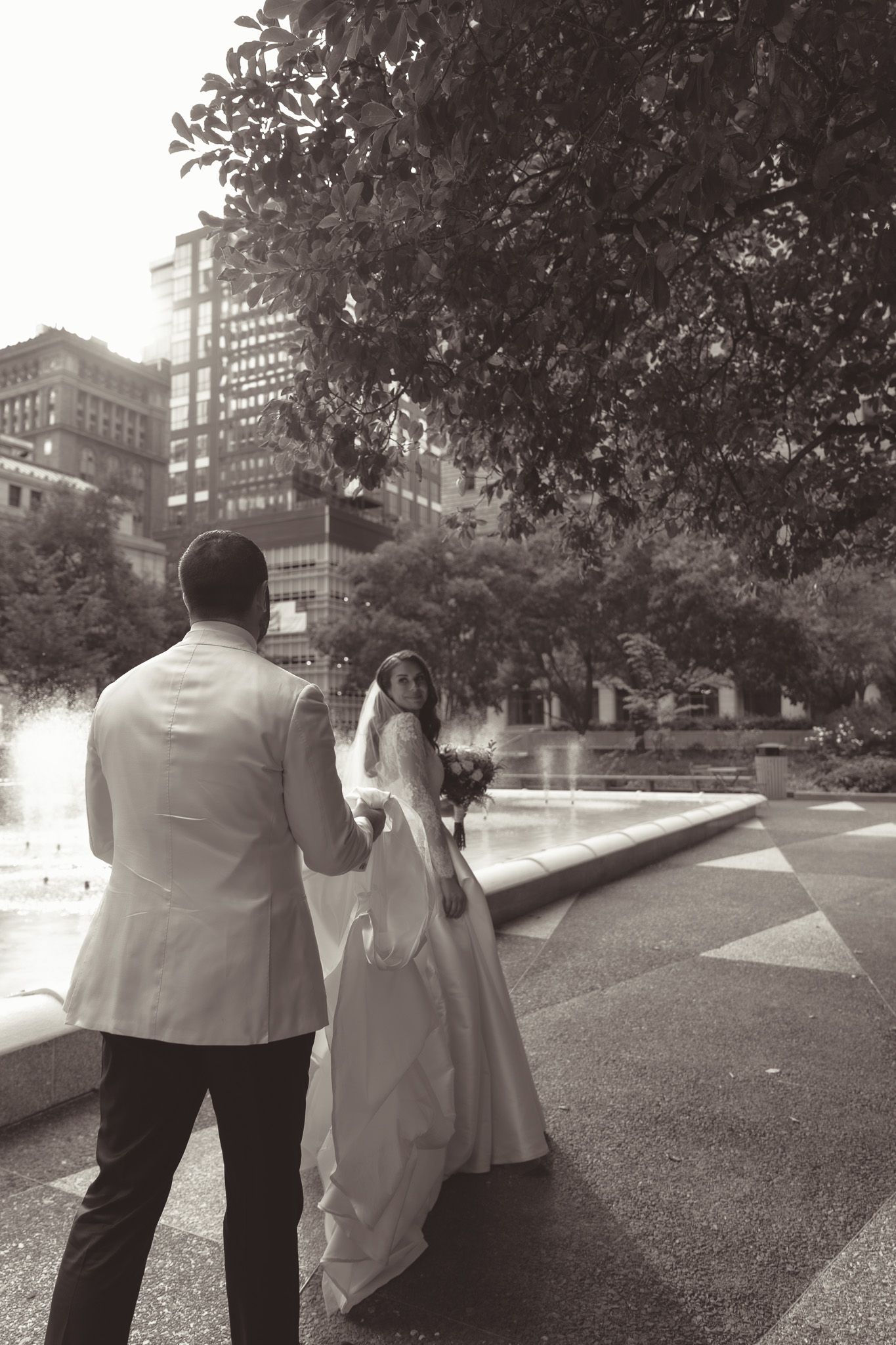 Black and white photo of couple in wedding attire against urban backdrop with trees in downtown pittsburgh, pa.