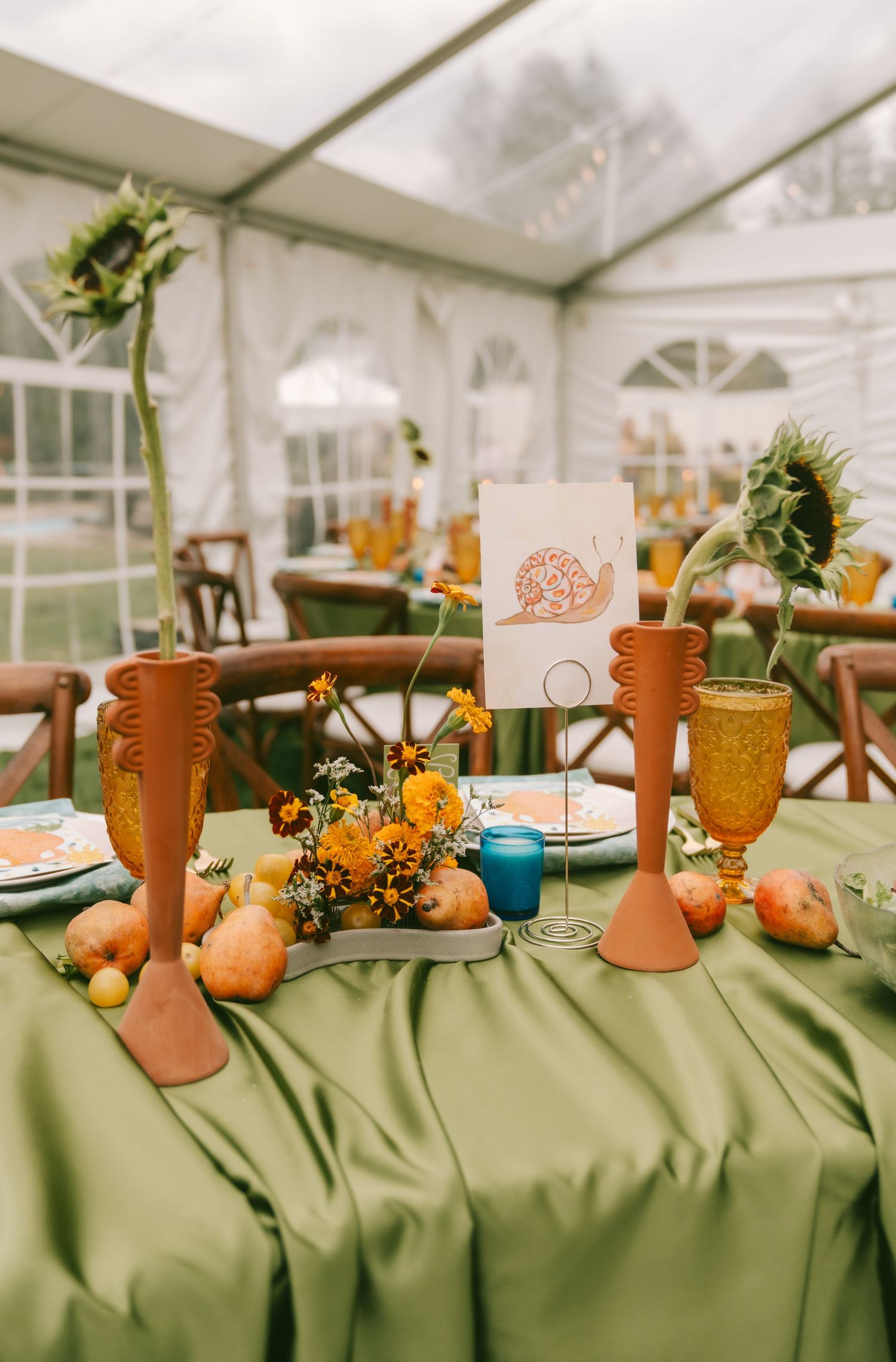 Wedding reception table decorated with terracotta vases, orange flowers, and sage green linens.