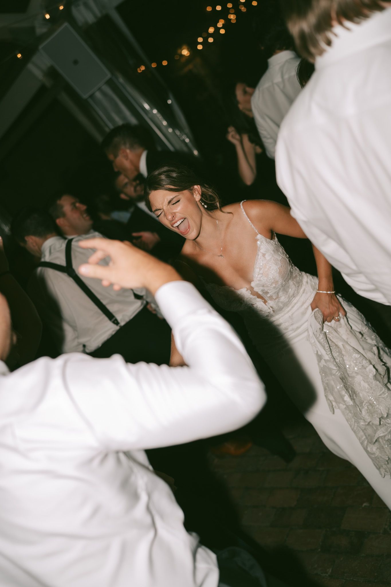 A bride and groom dance together at their wedding reception with guests visible in the background.
