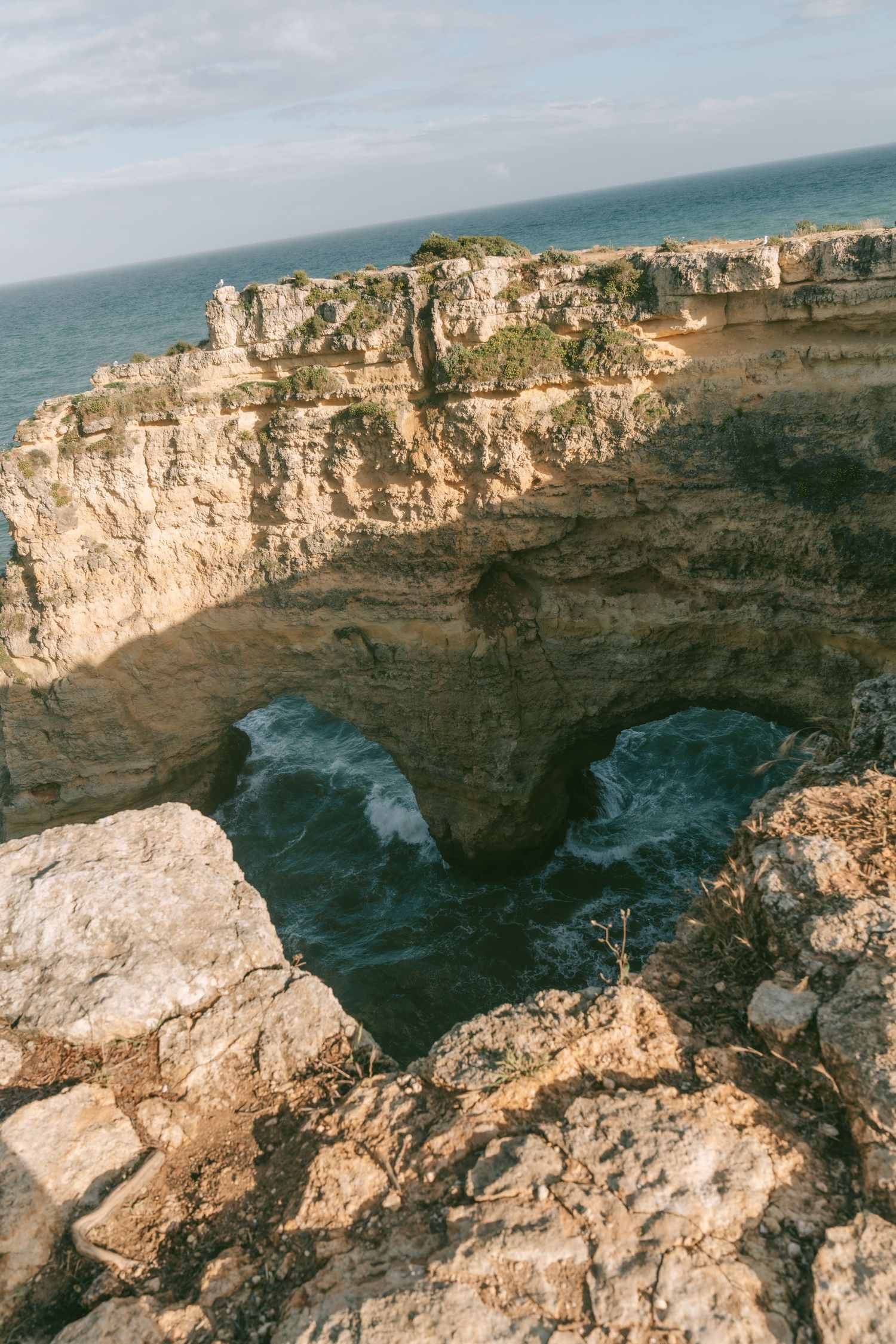 Heart-shaped natural rock arch over turquoise ocean waves along rugged limestone cliffs in Algarve, Portugal.