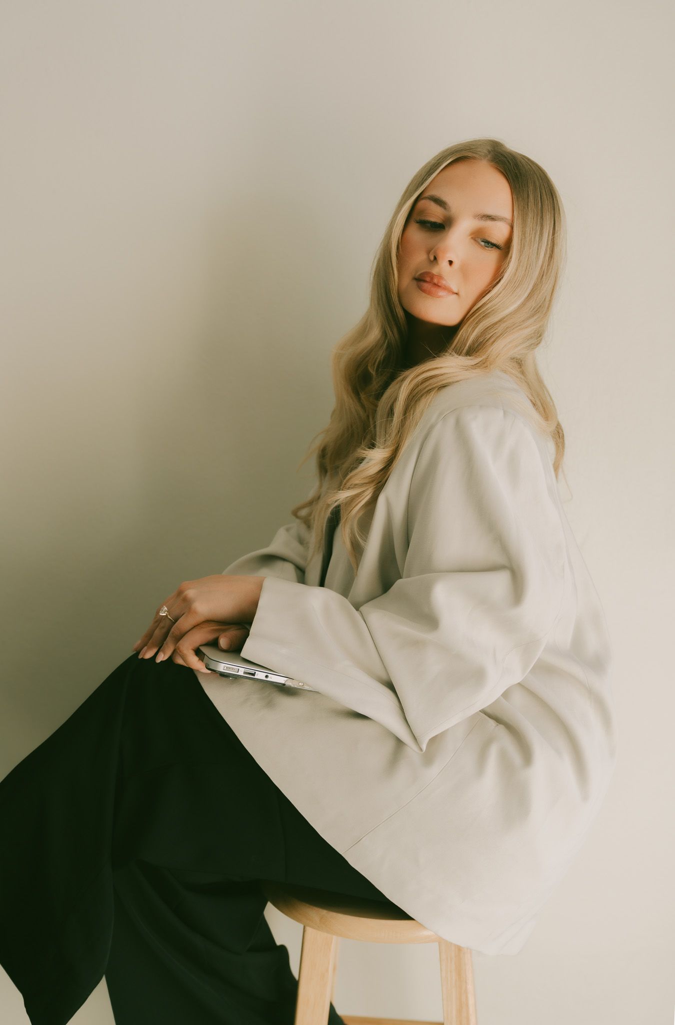 Fashion portrait in minimalist style featuring cream blazer and black pants against neutral wall.