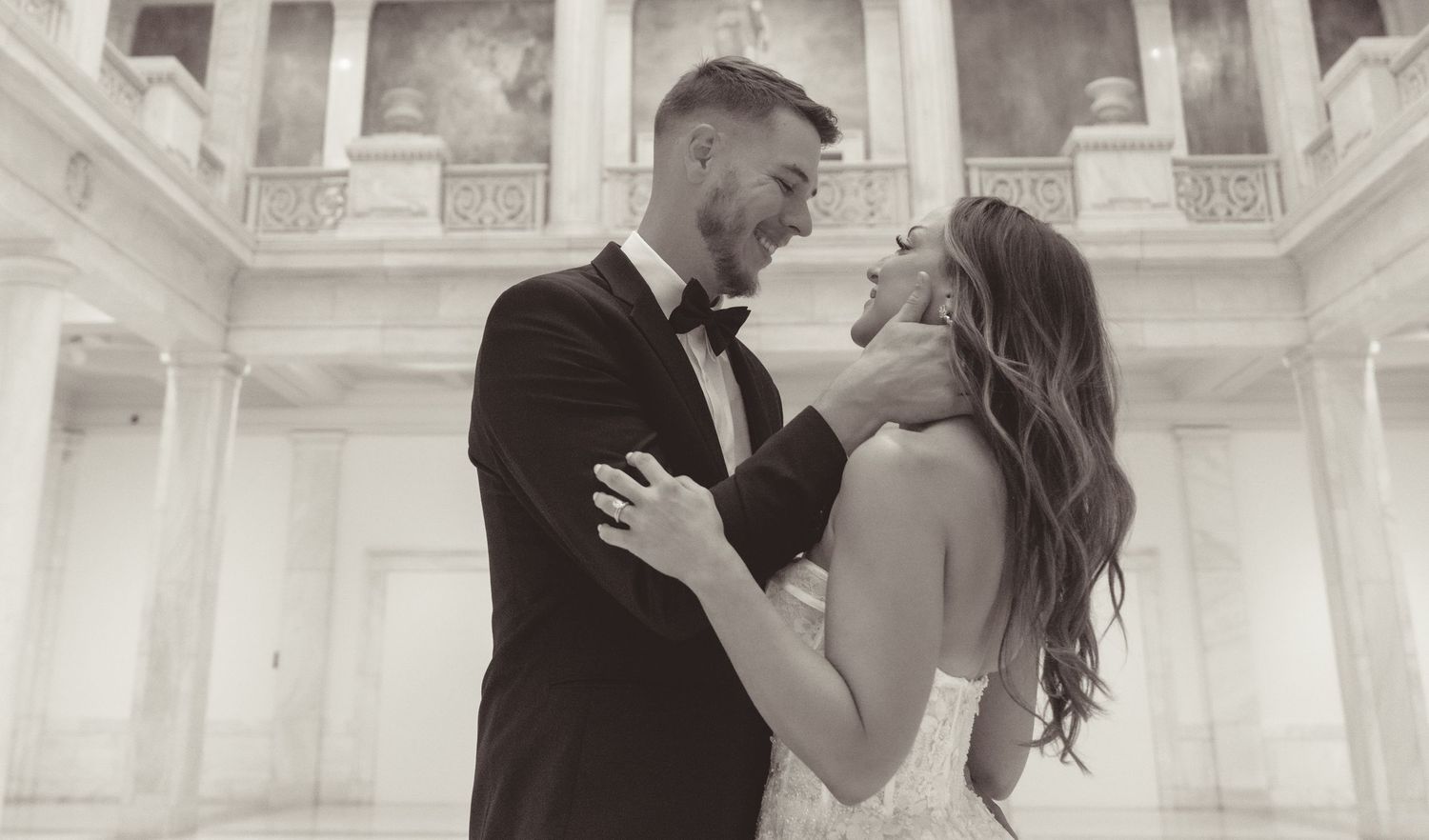 Newlyweds embracing in an elegant white columned interior venue.