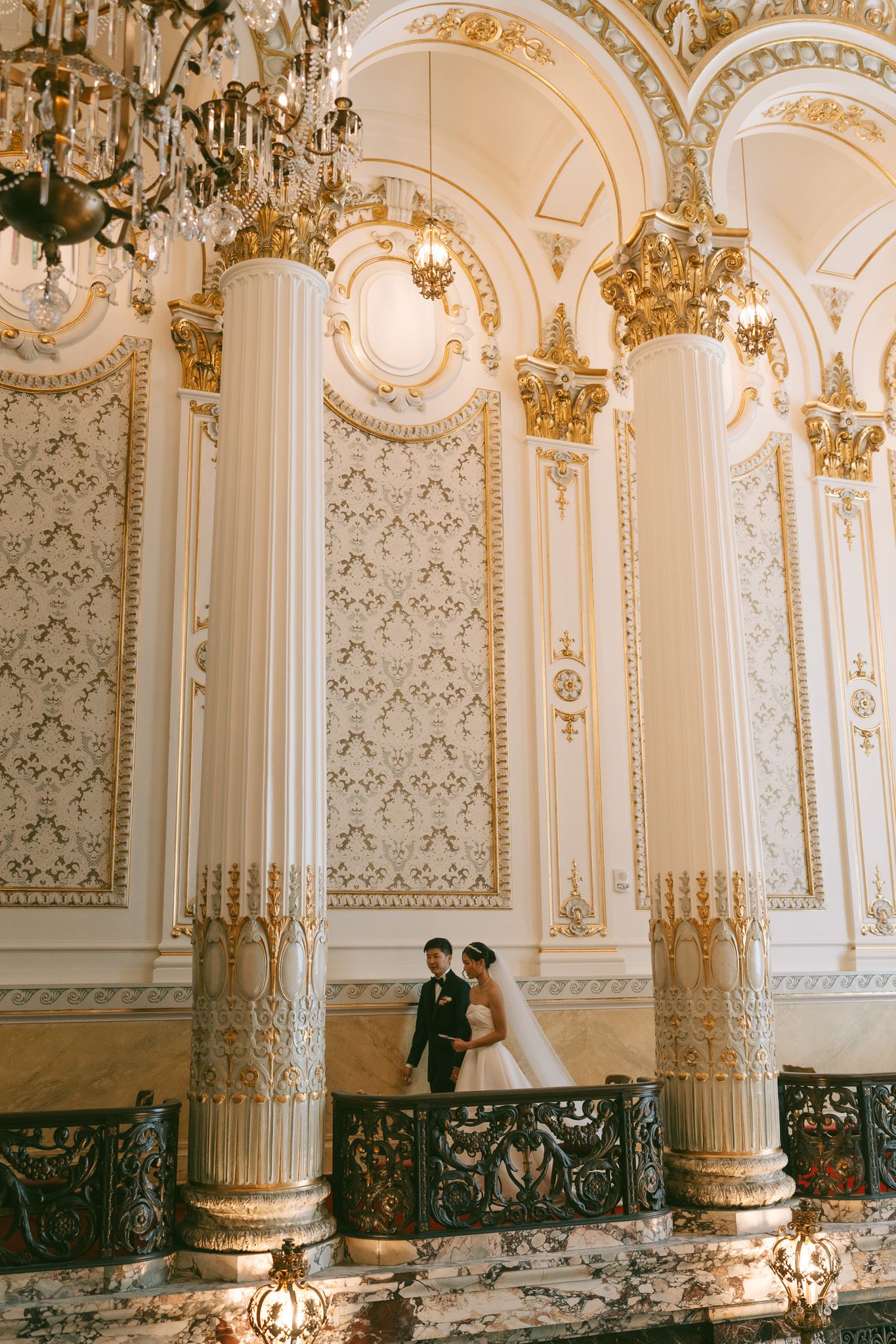 Wedding couple poses in ornate baroque palace hall with gilded columns and crystal chandeliers in Pittsburgh, PA.