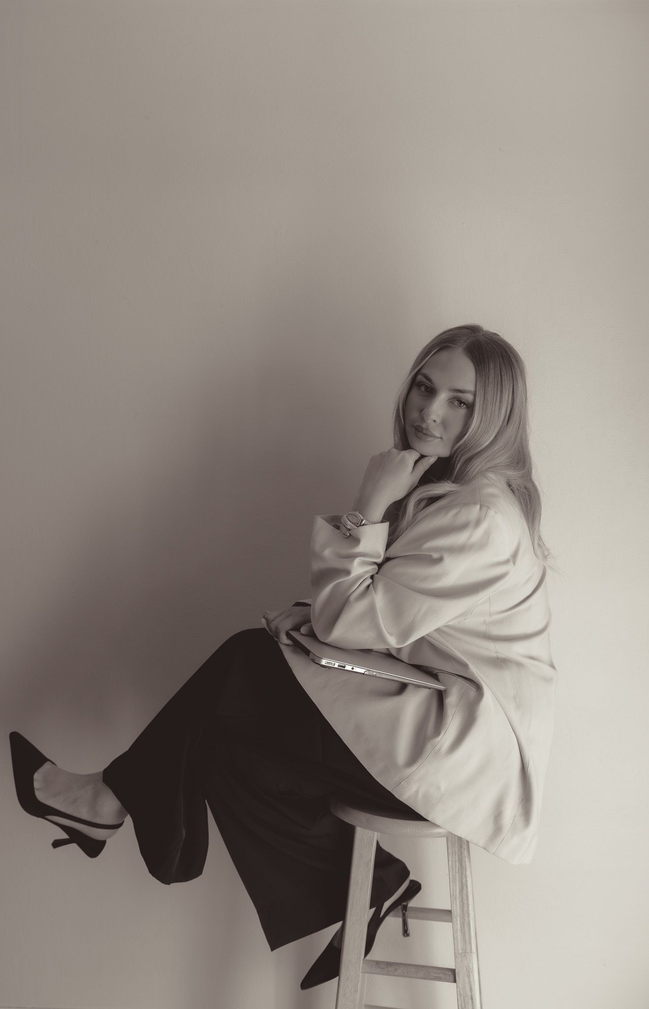Artistic portrait of person in oversized white sweater sitting on stool against neutral background.