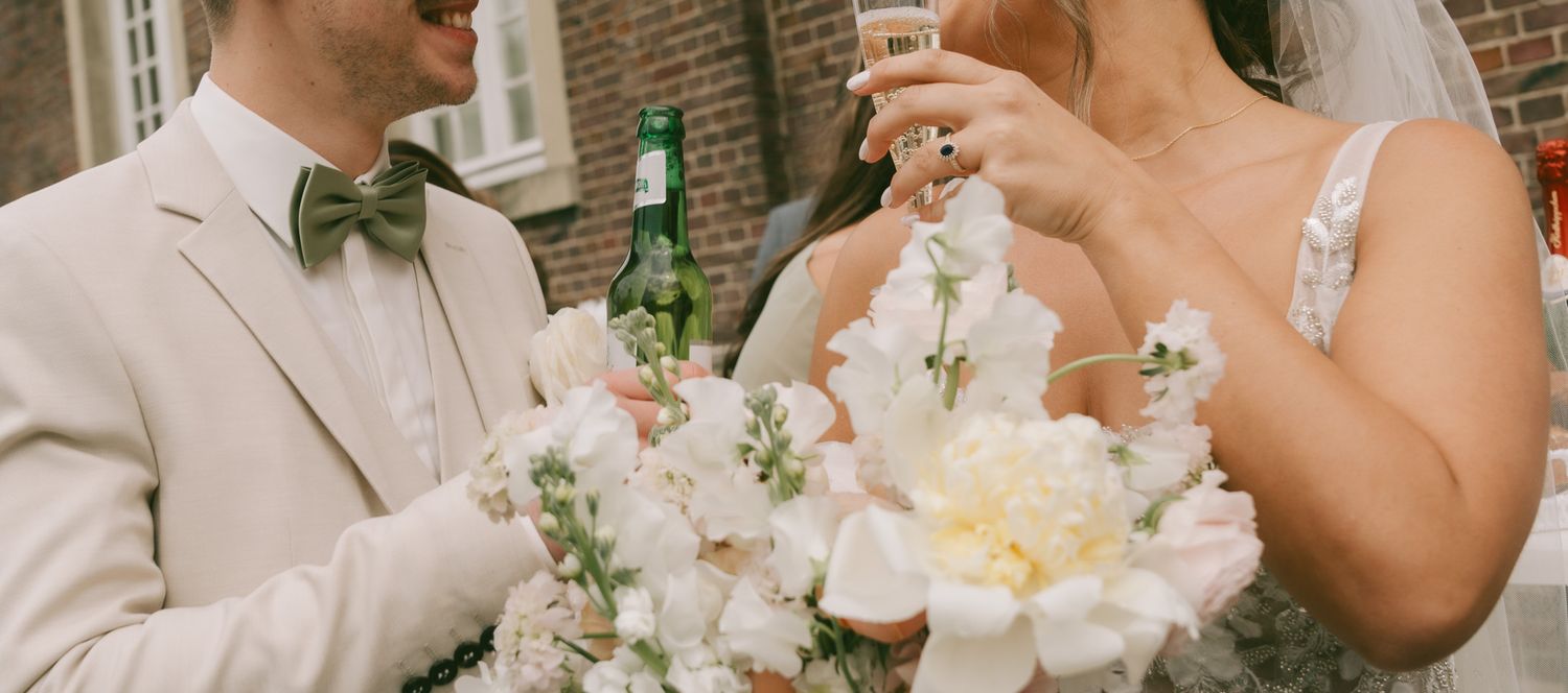 Wedding couple toasts with drinks while holding elegant floral bouquets in Germany.