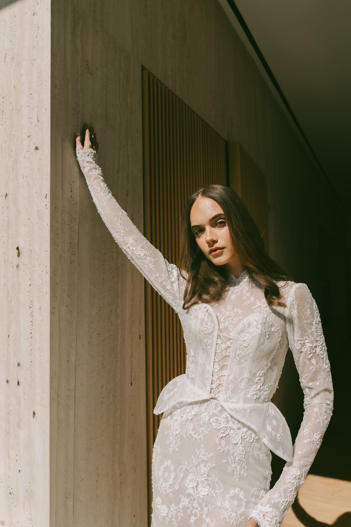 Elegant Eden Aharon lace wedding dress with long sleeves and fitted silhouette shown against a minimalist concrete wall in NYC.