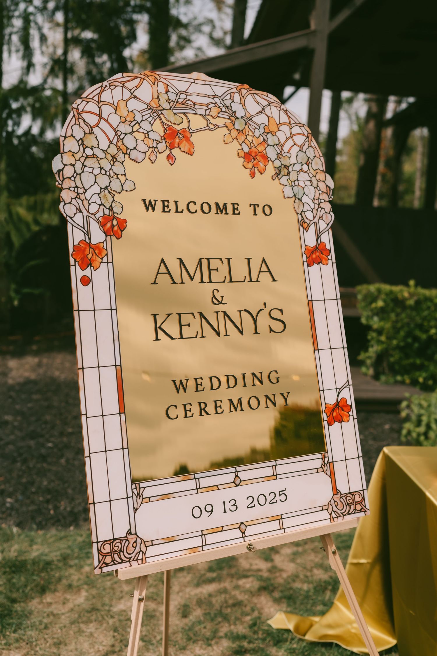 Three elegant wedding ceremony signs with floral designs and gold accents displayed outdoors against a natural backdrop.